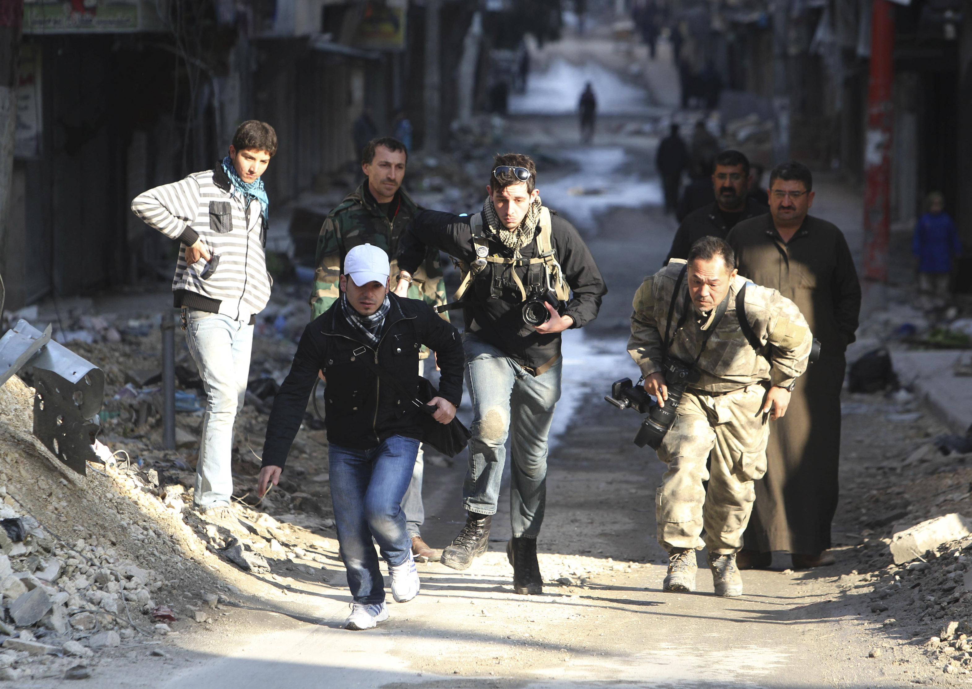 Journalists Bryn Karcha (C) of Canada and Toshifumi Fujimoto (R) of Japan run for cover next to an unidentified fixer in a street in Aleppo's district of Salaheddine on 29 December 2012