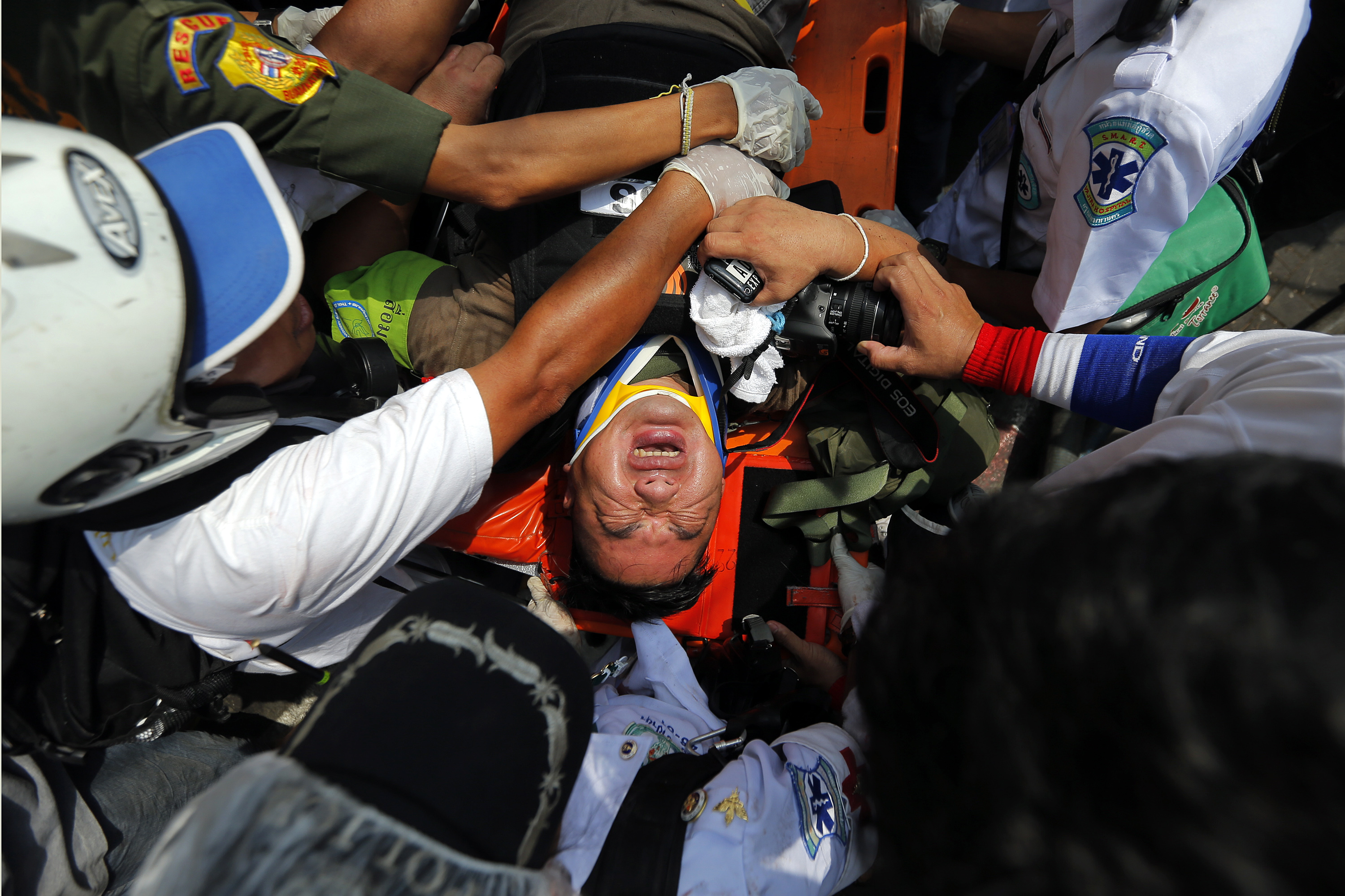An injured reporter is taken to an ambulance during clashes between the police and anti-government protesters near the Government House in Bangkok, 18 February 2014