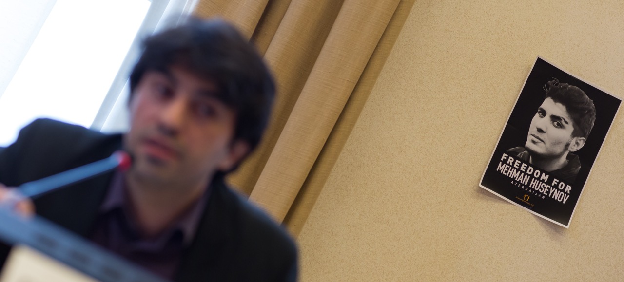 Emin Huseynov speaking at a side-event on human rights in Azerbaijan, while a poster of his brother Mehman Huseynov is seen behind him, during the 34th session of the Human Rights Council in Geneva, 7 March 2017