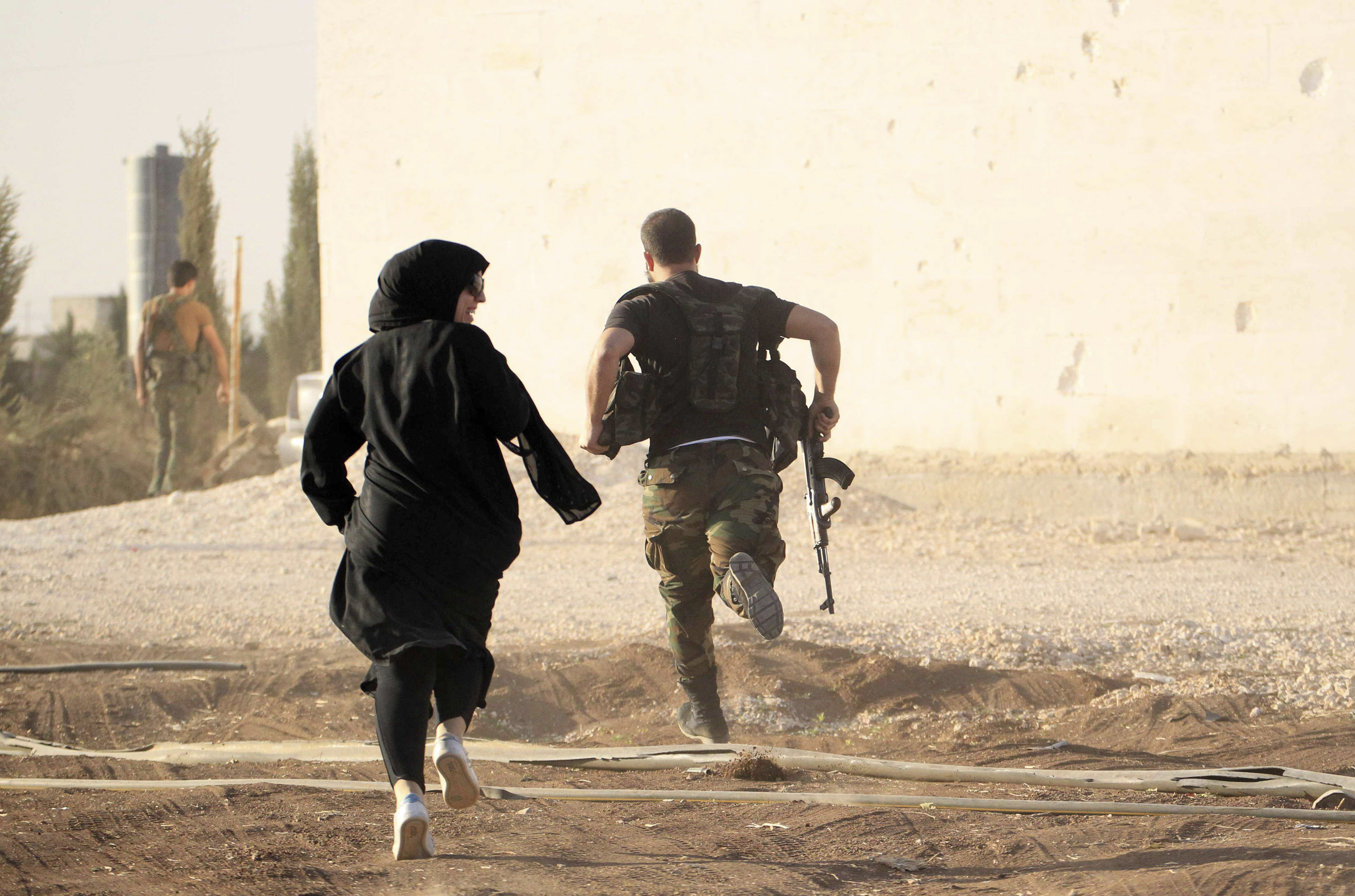 A woman reporter runs with a rebel fighter to avoid snipers at the frontline against the Islamic State fighters in Aleppo's northern countryside, 10 October 2014