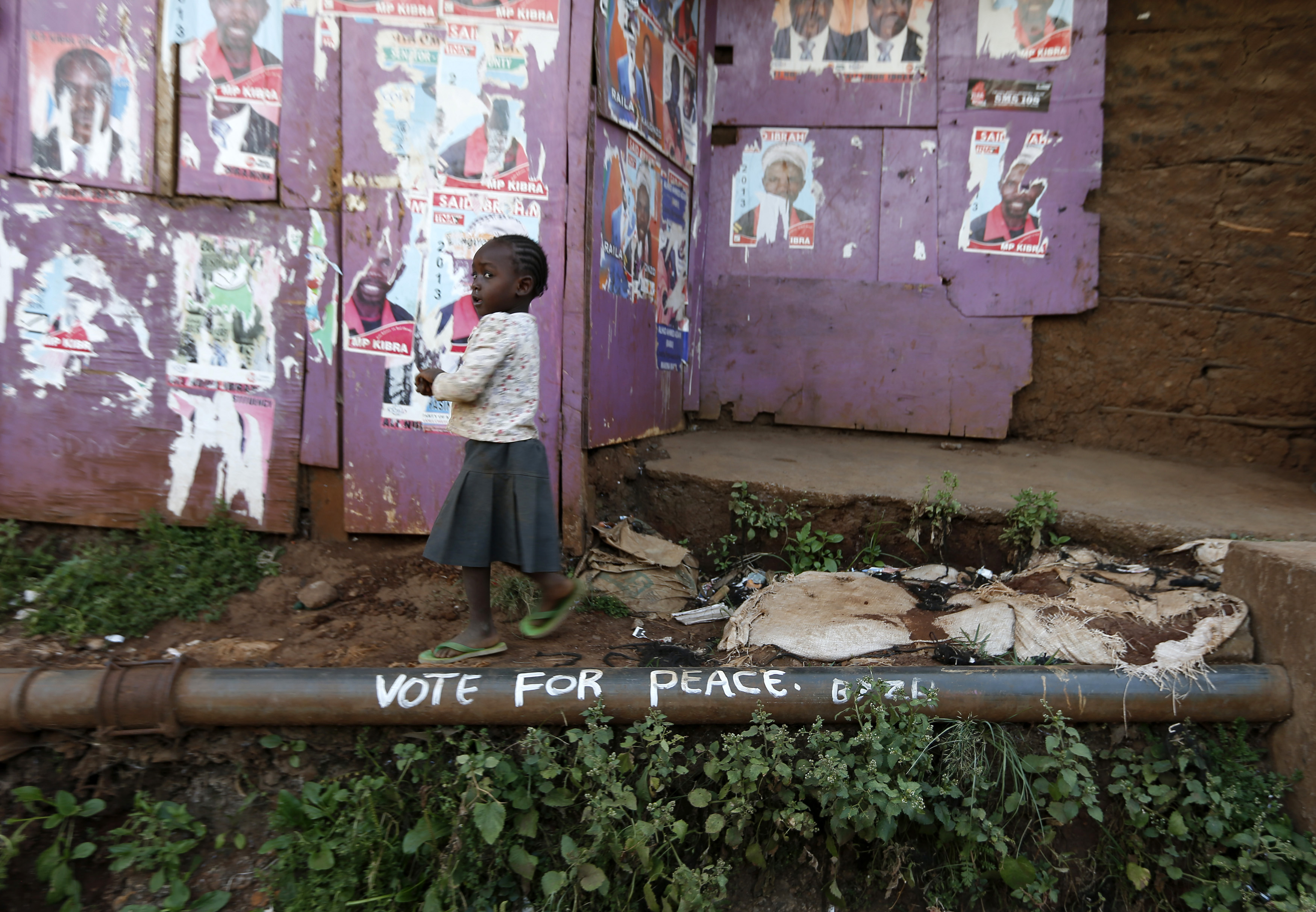 Une jeune fille passe devant des affiches électorales et un slogan appelant à la paix dans le bidonville de Kibera à Nairobi le 7 mars 2013