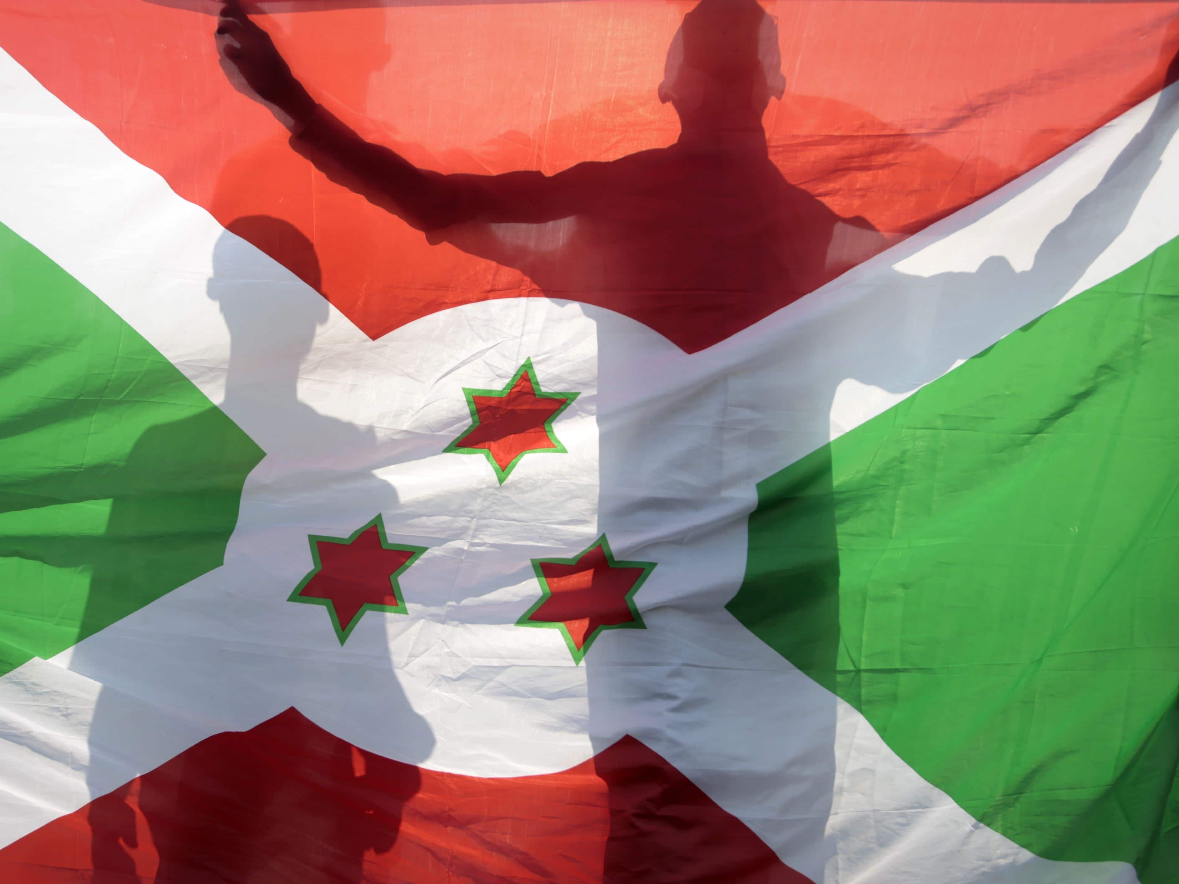 People are silhouetted behind the Burundi national flag in Bujumbara, 9 June 2015, AP Photo/Gildas Ngingo