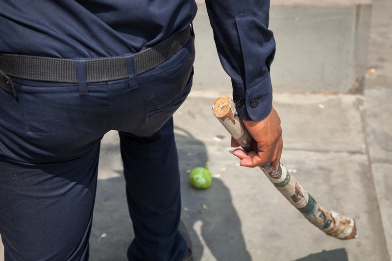 Police officer carrying a newspaper-wrapped piece of wood which was used as a weapon against peaceful demonstrators during Labour Day in Phnom Penh, 1 May 2014, Demotix/Erika Pineros
