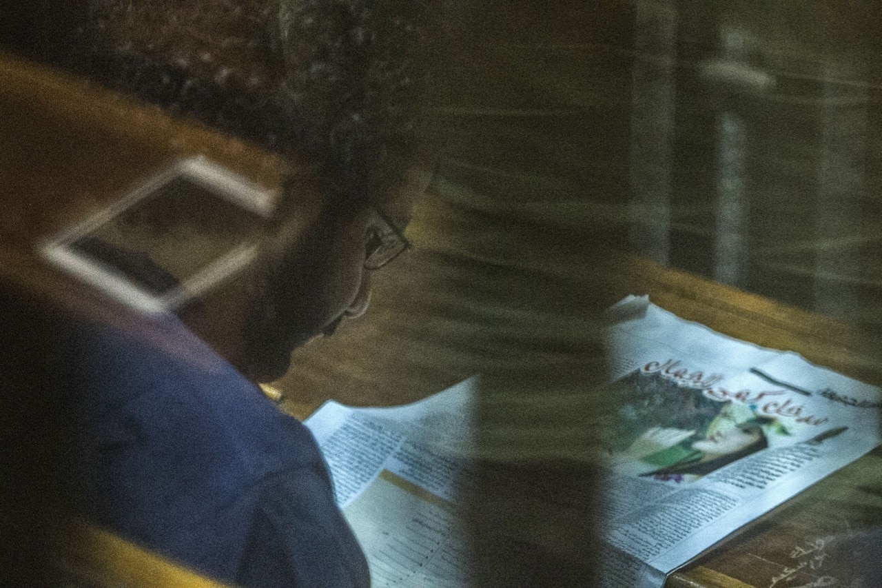 Egyptian activist and blogger Alaa Abdel Fattah reads a newspaper during his trial for insulting the judiciary alongside 25 other defendants, in Cairo, 23 May 2015, KHALED DESOUKI/AFP/Getty Images