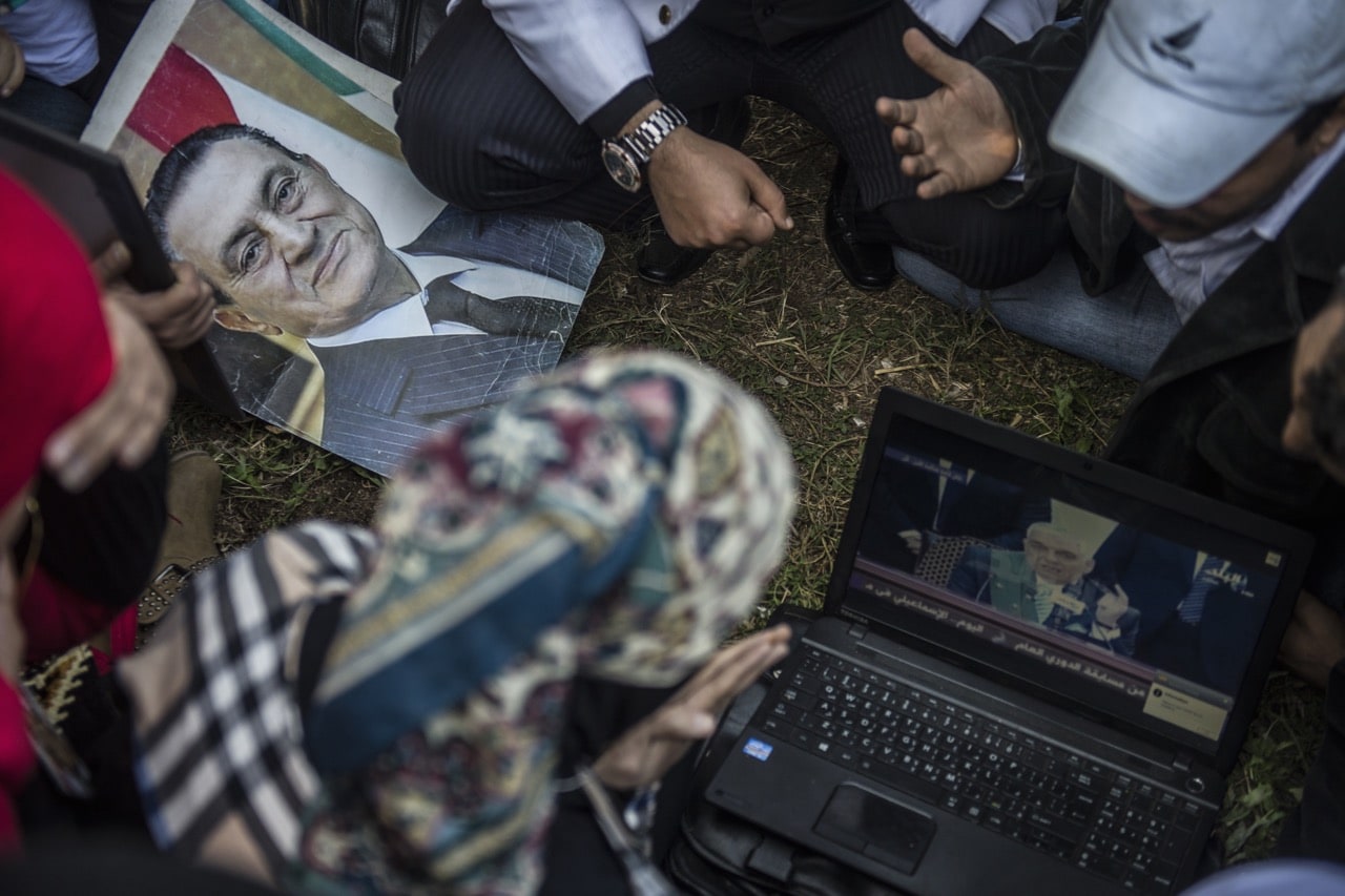 Supporters of Egypt's former president Hosni Mubarak (portrait) watch his trial live on a laptop outside Maadi military hospital in Cairo, 29 November 2014, KHALED DESOUKI/AFP/Getty Images