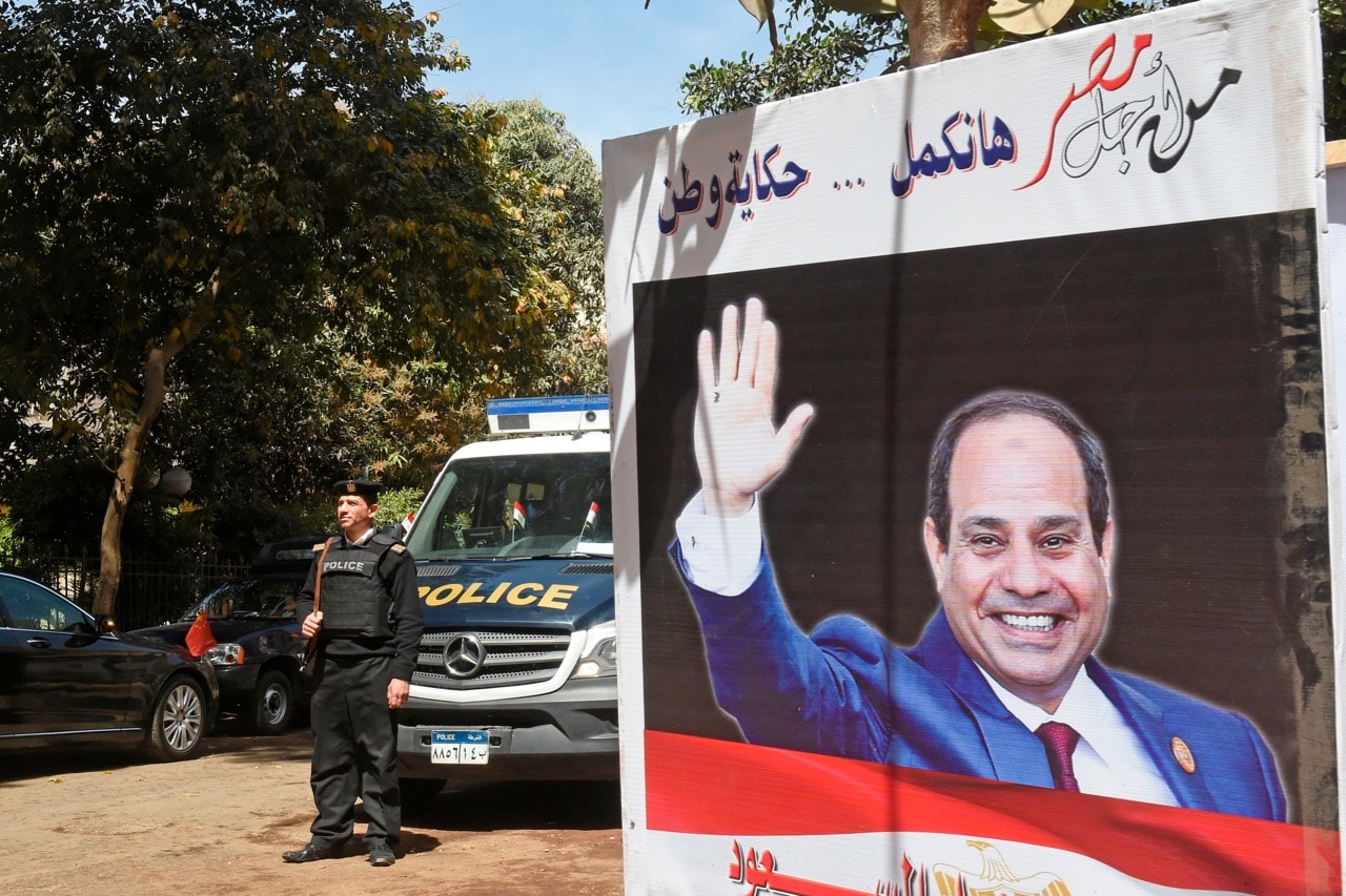 Egyptian policemen stand guard outside a polling station with an electoral banner depicting incumbent President Abdel Fattah al-Sisi in Cairo, 26 March 2018, KHALED DESOUKI/AFP/Getty Images