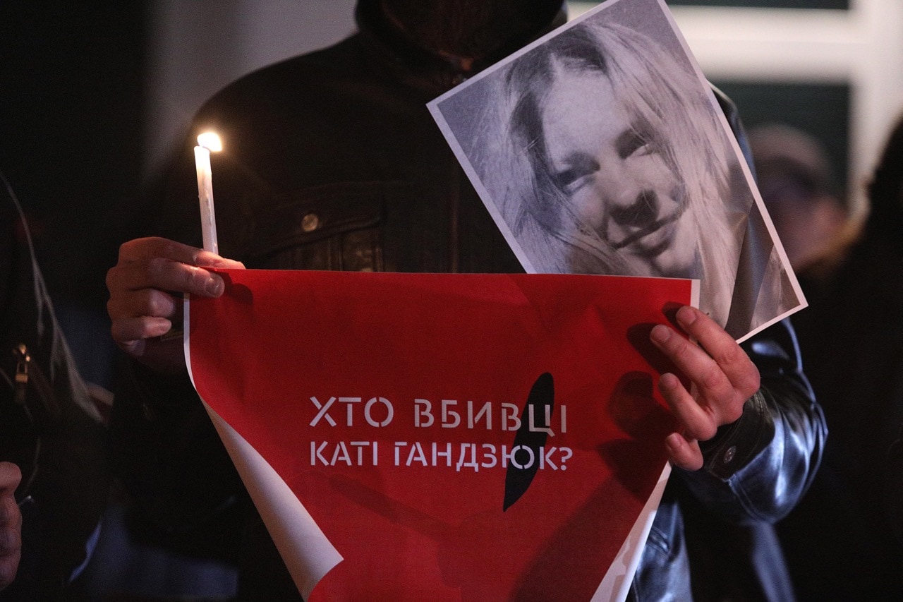 A demonstrator holds a photo of anti-corruption activist Kateryna Handziuk, a candle and a placard reading in Ukrainian "Who are the Murderers of Katia Handziuk?" during a rally outside the Interior Ministry in Kyiv, 4 November 2018, Danil Shamkin / Barcroft Media via Getty Images