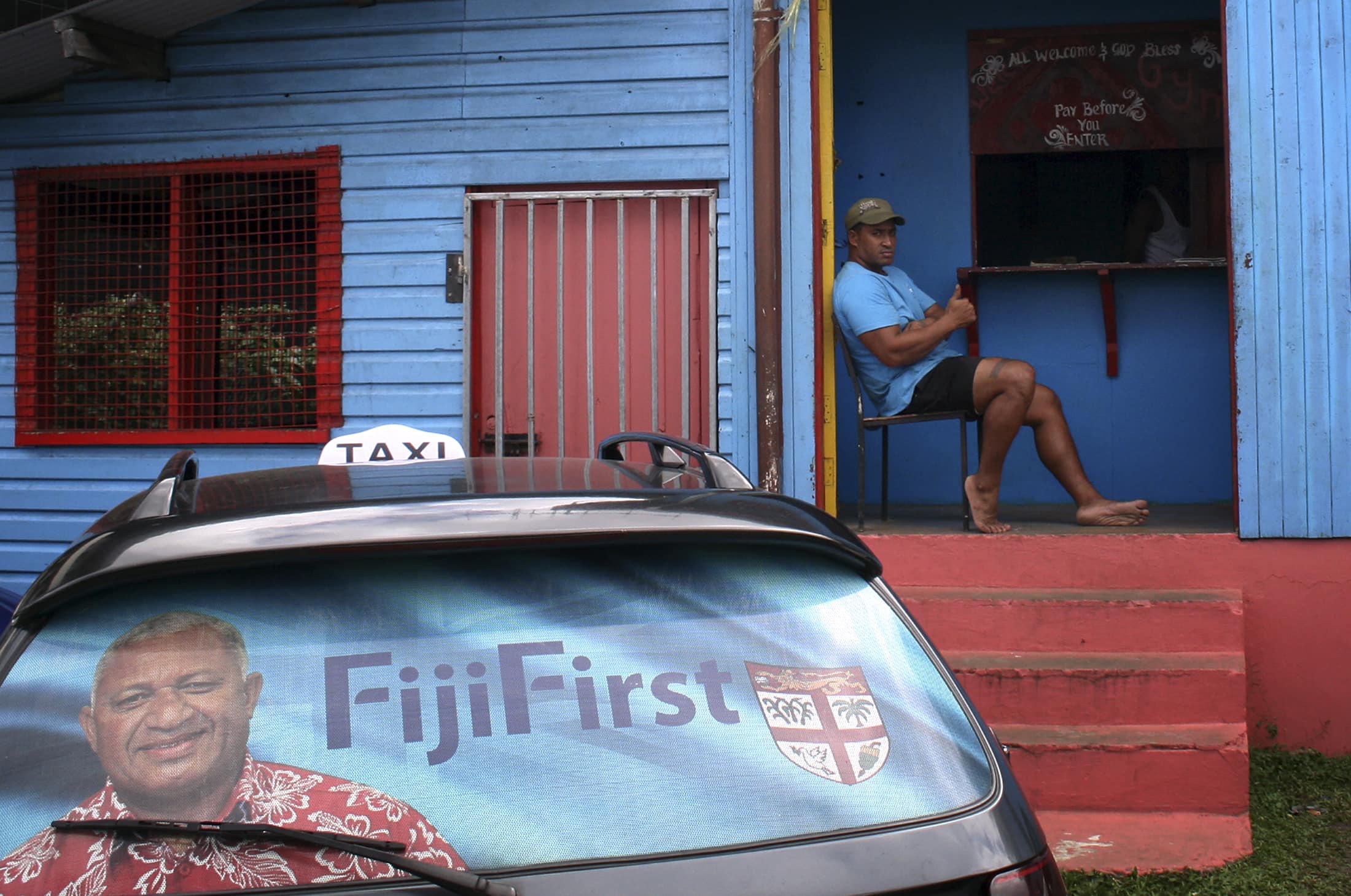 An election poster for Voreqe "Frank" Bainimarama can be seen in the rear window of a taxi as a man gestures from the doorway of a local gymnasium in the Fiji capital of Suva, 26 August 2014, REUTERS/Lincoln Feast