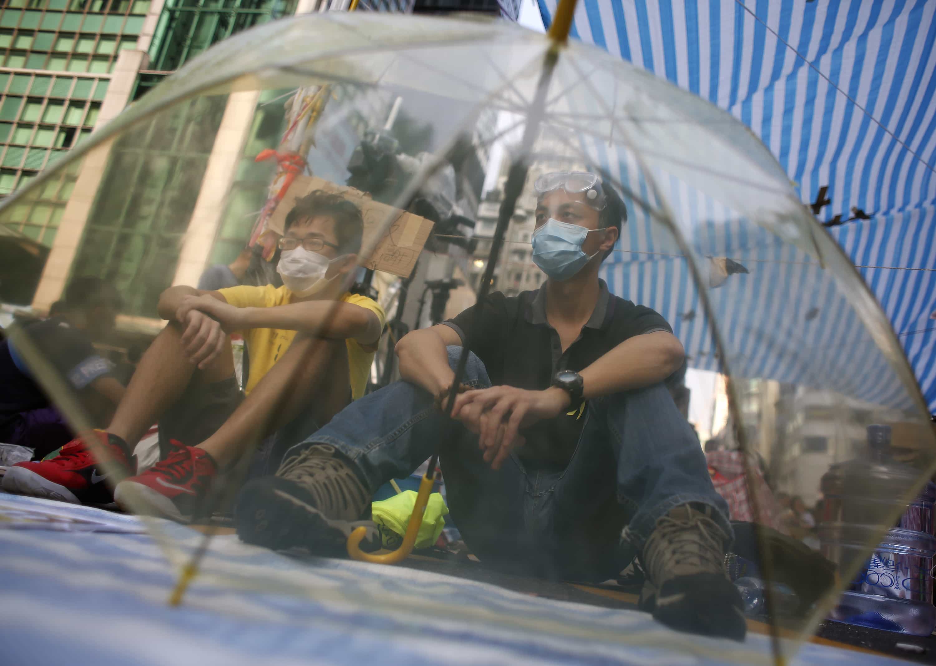 Pro-democracy protesters sitting behind an umbrella guard a tent from possible attacks by anti-Occupy Central protesters in Hong Kong, 5 October 2014, REUTERS/Bobby Yip