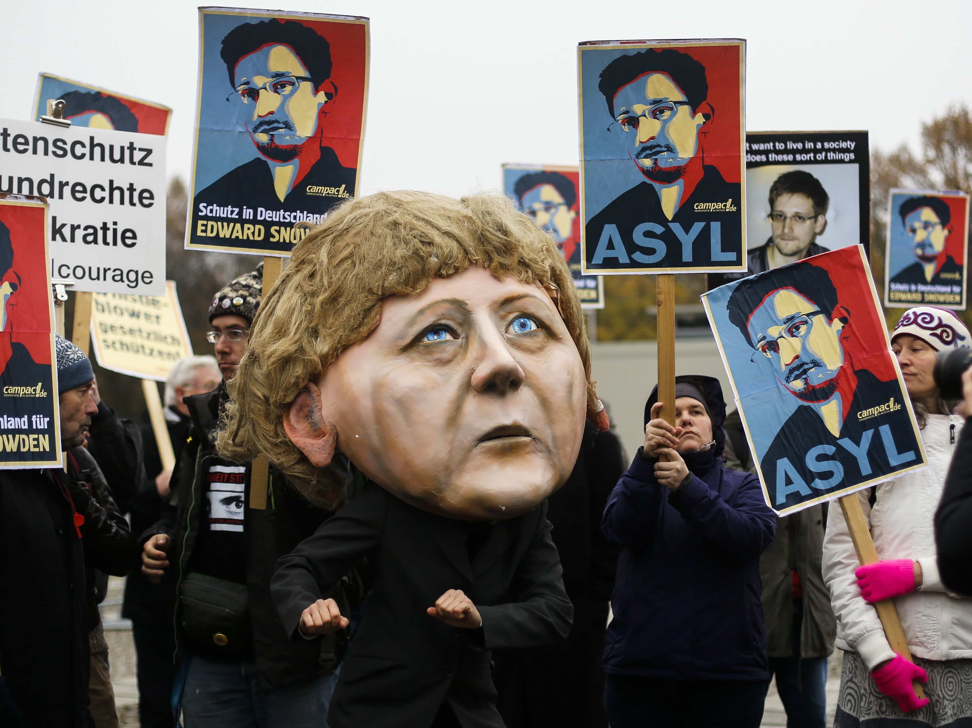 A demonstrator with a mask depicting German Chancellor Angela Merkel and others holding posters of Snowden take part in a November 2013 protest outside the German parliament building in Berlin, AP Photo/Markus Schreiber