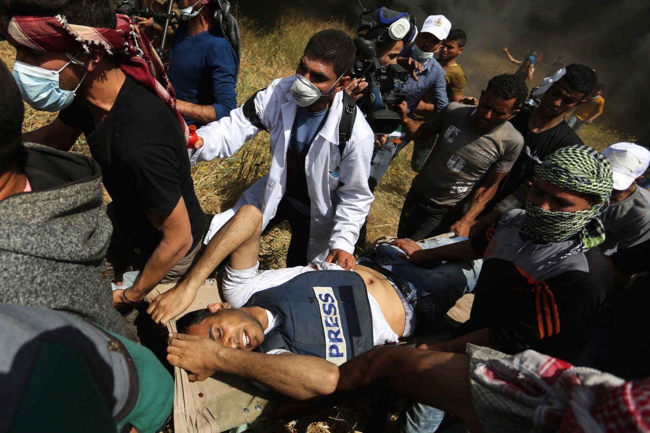 Palestinians carry journalist Yaser Murtaja, shot in the abdomen by the Israeli military while wearing a clearly marked press jacket in a demonstration, east of Khan Yunis, Gaza, 6 April 2018, Ashraf Amra/Anadolu Agency/Getty Images