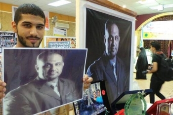 Jaffar Al-Demstani holding a photo of his imprisoned father, BCHR