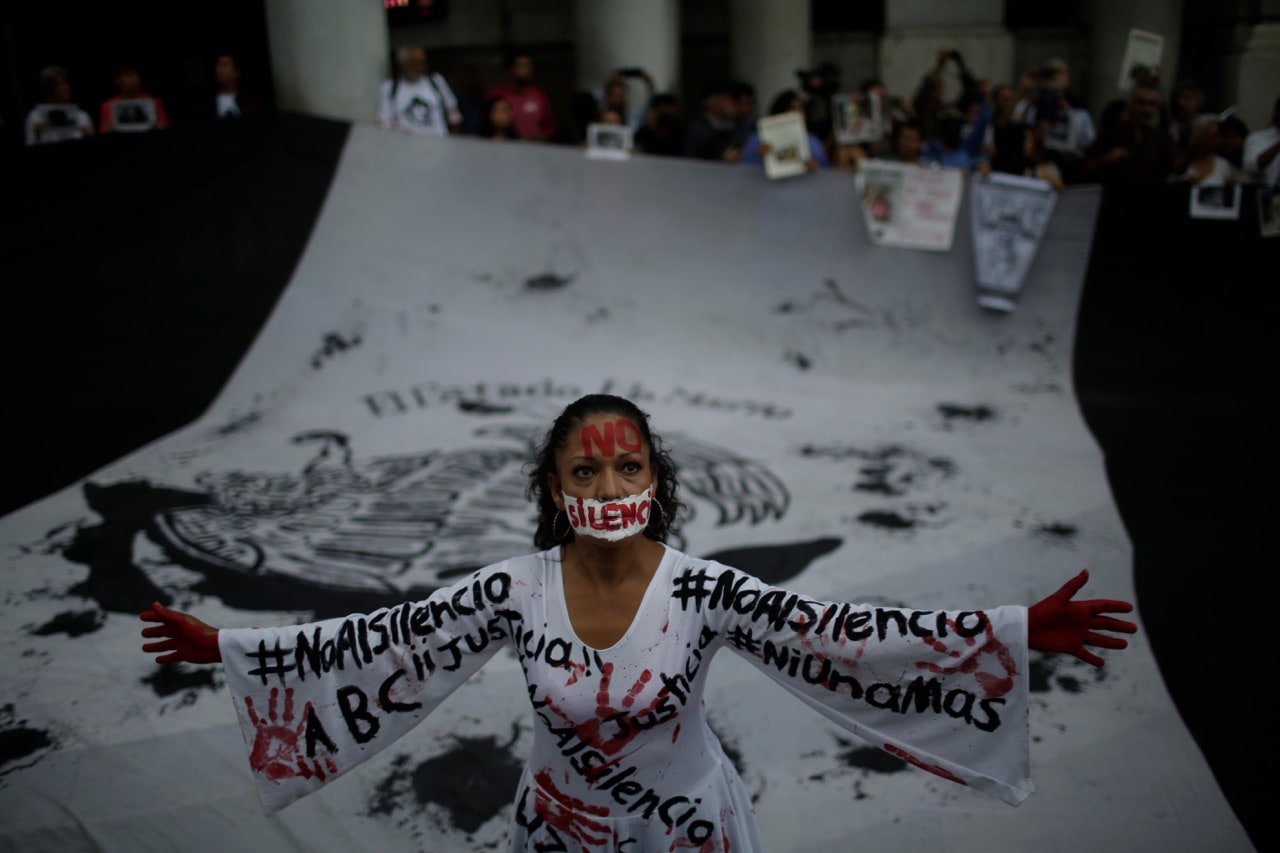 A woman wearing a dress that reads 'no to silence' stands in front of a flag during a demonstration to end violence against journalists in Mexico at the Interior Ministry in Mexico City, 15 June 2017, Miguel Tovar/LatinContent/Getty Images