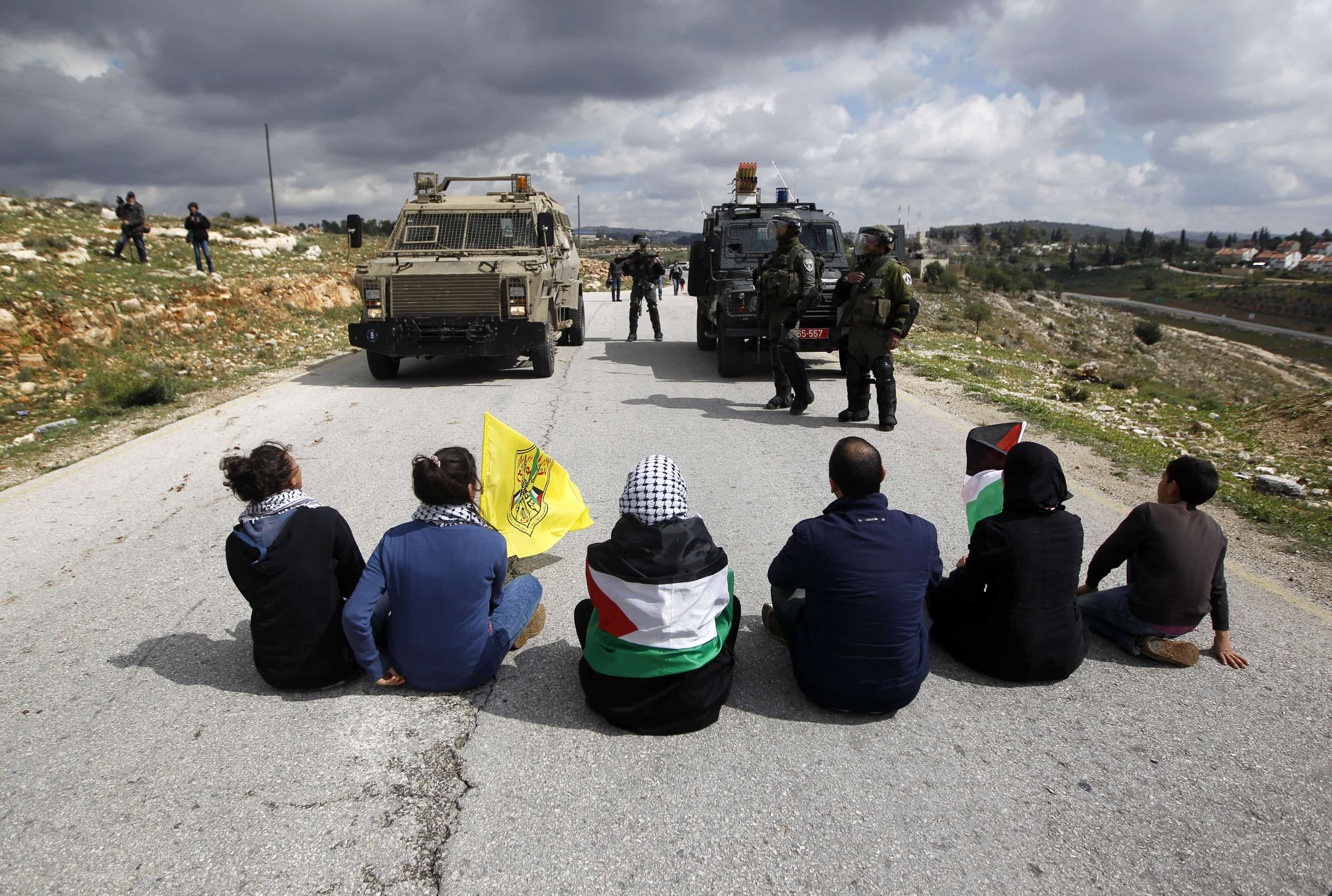 Palestinian activists hold flags as they sit on a road in front of Israeli military vehicles at a weekly protest against Jewish settlements, in the West Bank village of Nabi Saleh, near Ramallah on 14 March 2014 , REUTERS/Mohamad Torokman