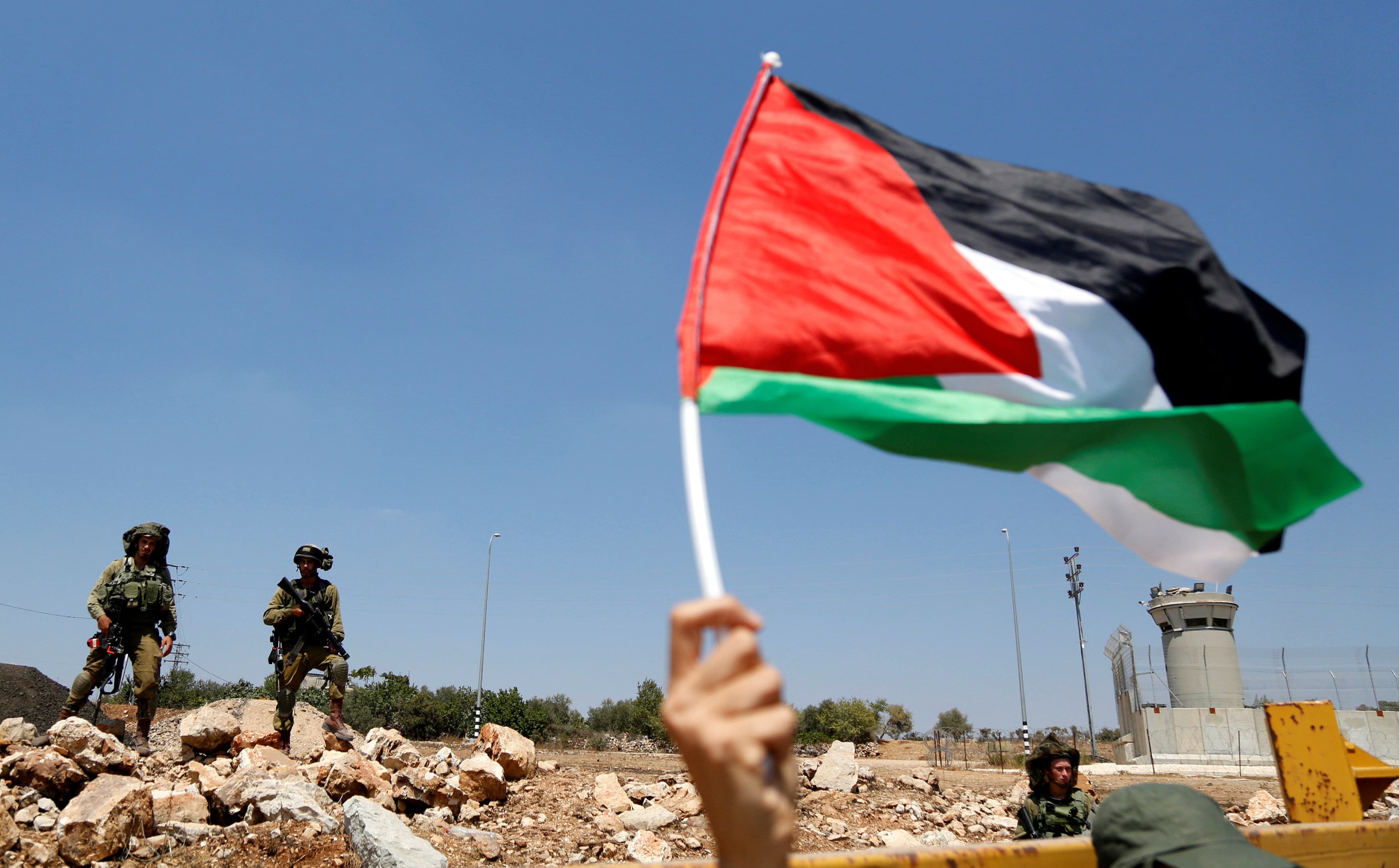 A demonstrator waves a Palestinian flag in front of Israeli soldiers during a protest in solidarity with Palestinian prisoners held in Israeli jails, in the West Bank village of Nabi Saleh, near Ramallah August 12, 2016,  REUTERS/Mohamad Torokman