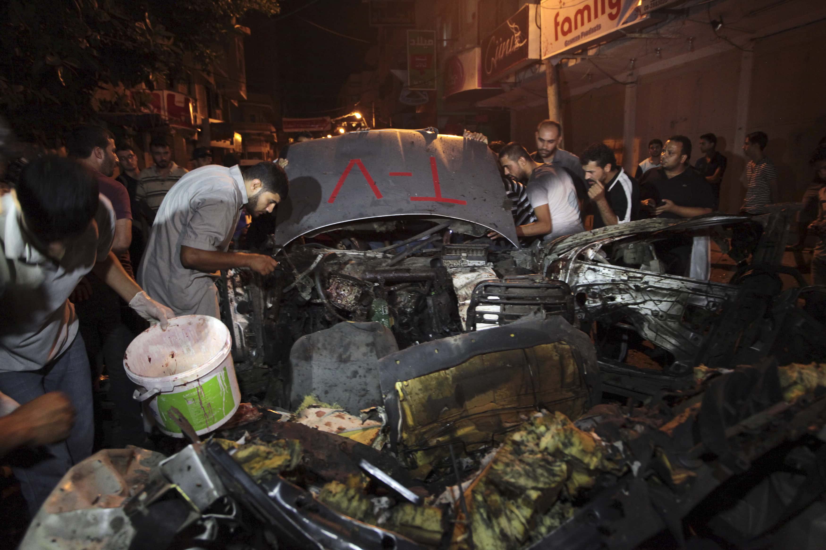 Palestinians inspect the remains of a car which police said was hit in an Israeli air strike in Gaza City on 9 July 2014, REUTERS/Ashraf Amrah