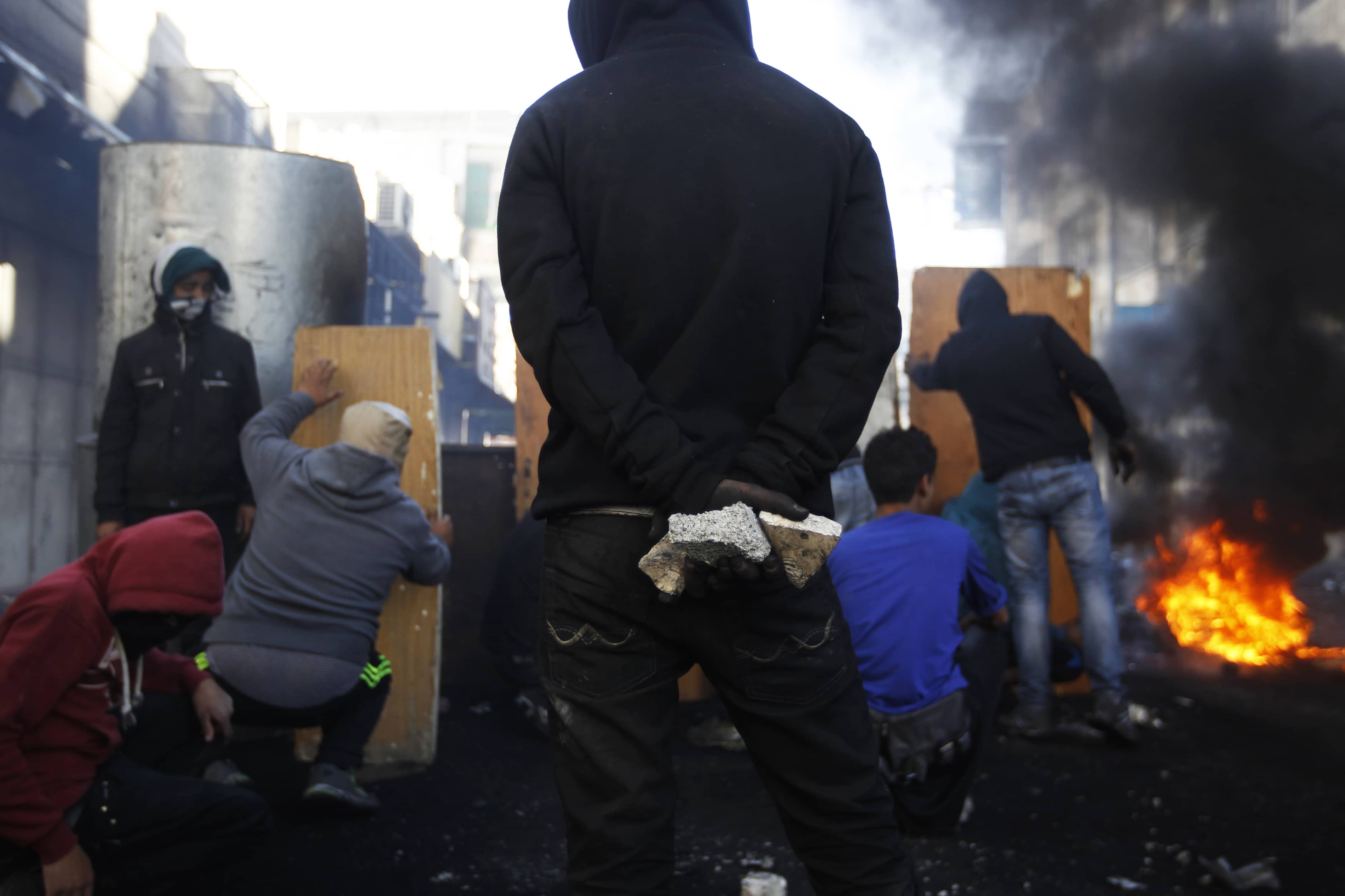 A Palestinian protester holds stones as others take cover during clashes with Israeli soldiers who fired live ammunition at the crowds following the funeral of Maysara Abu Hamdeya in Hebron, REUTERS/Ammar Awad