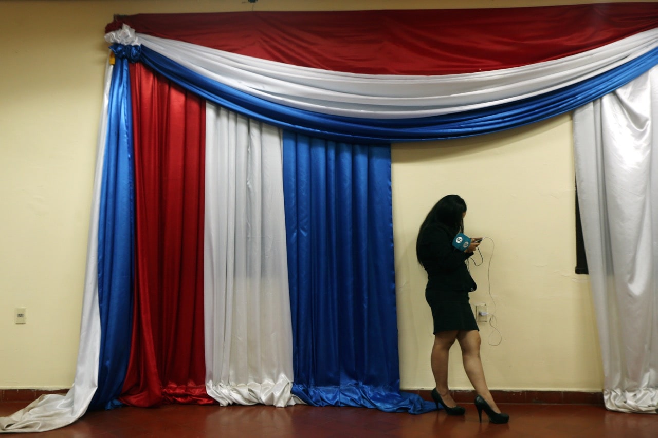 A journalist uses her phone next to a curtain with the colours of Paraguay's national flag as she waits for a news conference in Asuncion, Paraguay, 5 April 2017, REUTERS/Marcos Brindicci