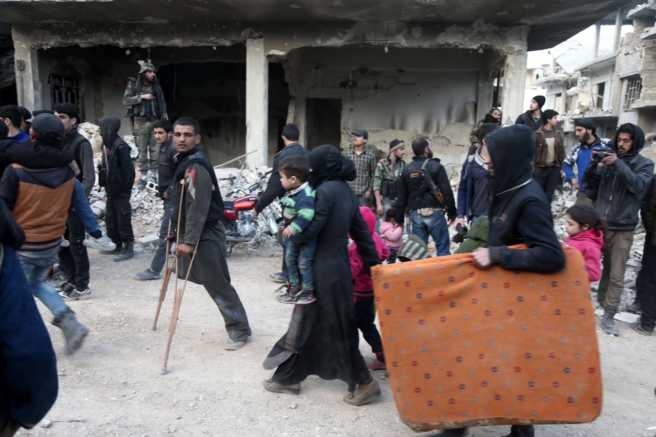 People walk down a destroyed street as they prepare to evacuate one of the few remaining rebel-held pockets in Arbin, in Eastern Ghouta, Syria, 24 March 2018, ABDULMONAM EASSA/AFP/Getty Images