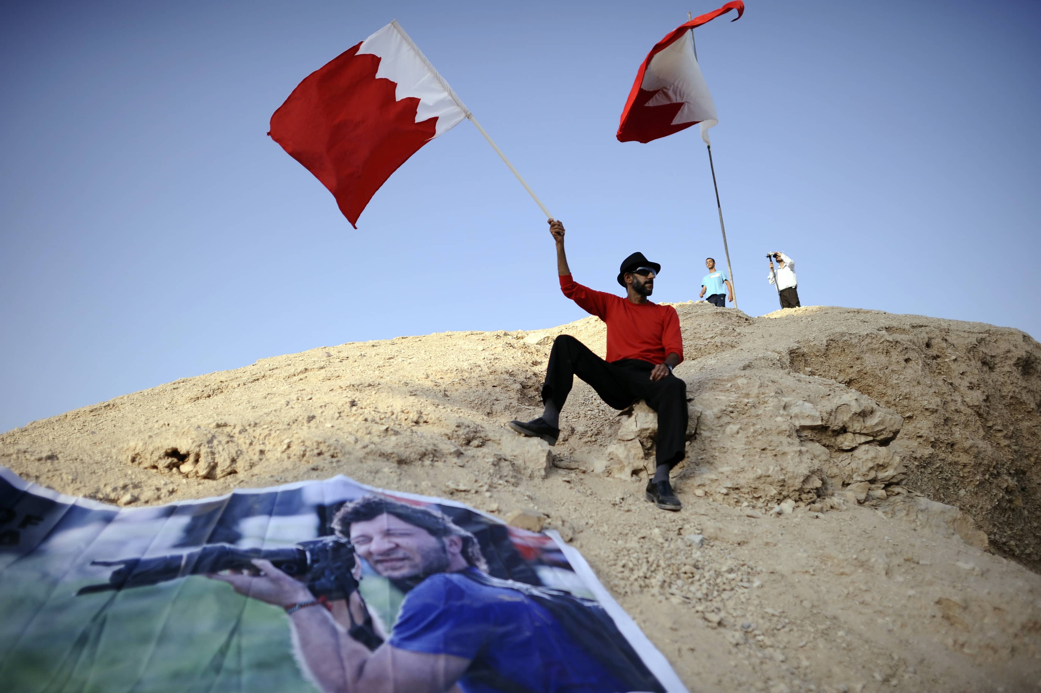 An anti-government protester waves a Bahraini national flag on November 2013 as he sits next to a poster showing news photographer Ahmed Humaidan, whose trial began on 12 February 2013. Humaidan received a 10-year jail sentence by a Bahraini court on 26 March 2014., REUTERS/Stringer