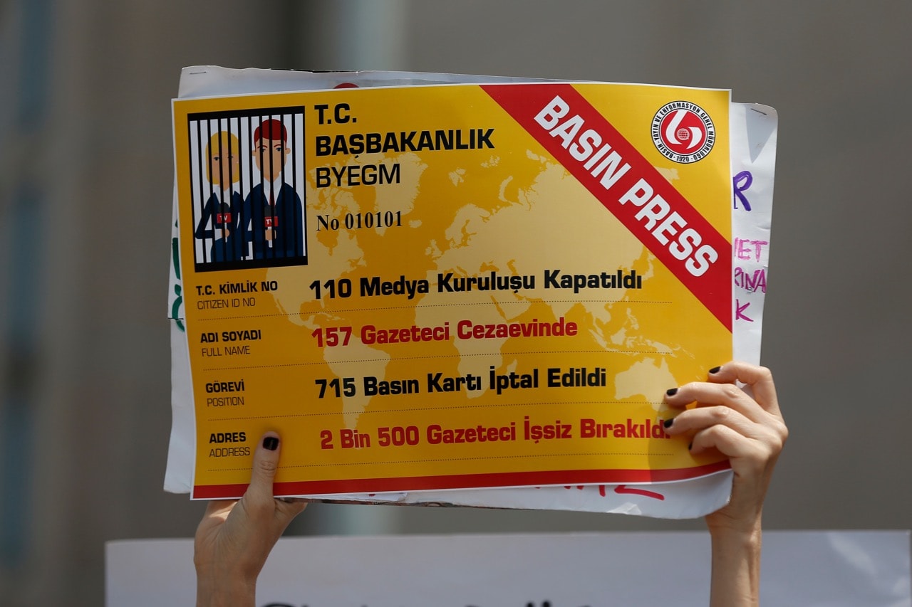 An activist holds a placard, made to look like a press card, that reads "110 media organizations closed, 157 journalists jailed, 715 press cards cancelled, 2.500 journalists fired" outside the court in Istanbul, 28 July 2017, AP Photo/Emrah Gurel