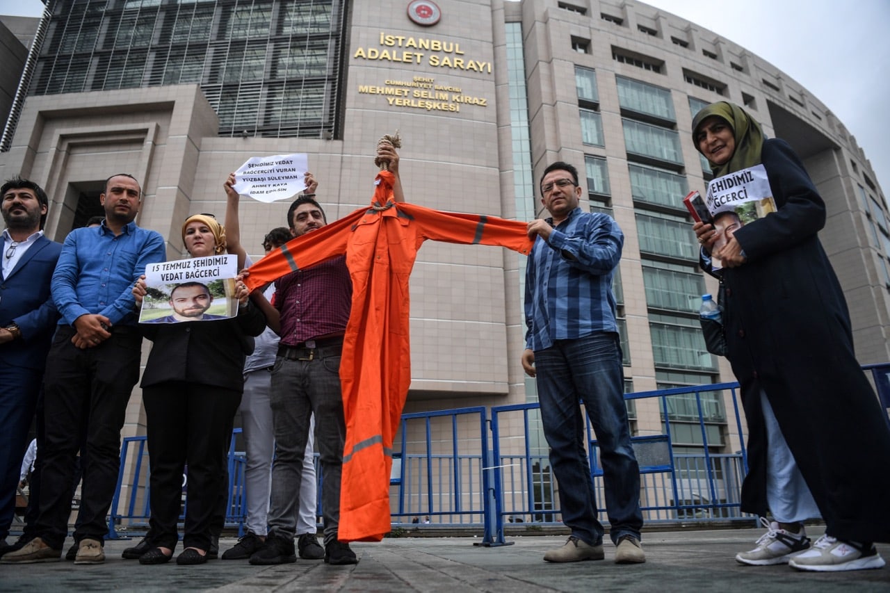 Relatives of Vedat Bagcerci, a victim of the 15 July 2016 failed coup, hold a uniform resembling the orange jumpsuits used at the US military prison at Guantanamo Bay, in front of a courthouse in Istanbul, 17 July 2017, OZAN KOSE/AFP/Getty Images