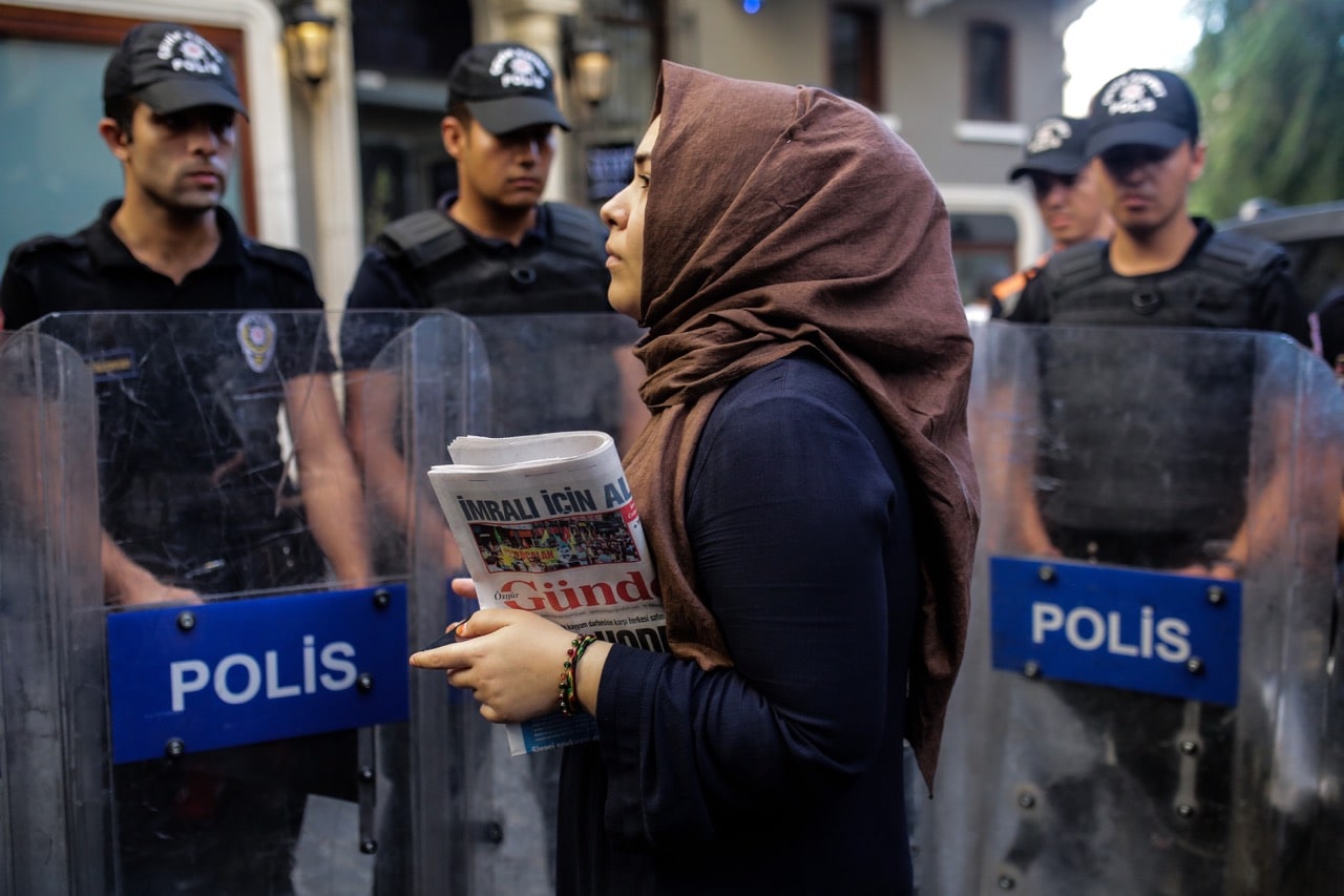 A woman holds a copy of the "Ozgur Gundem" newspaper in front of a police barricade on 16 August 2016 in Istanbul, Turkey, YASIN AKGUL/AFP/Getty Images