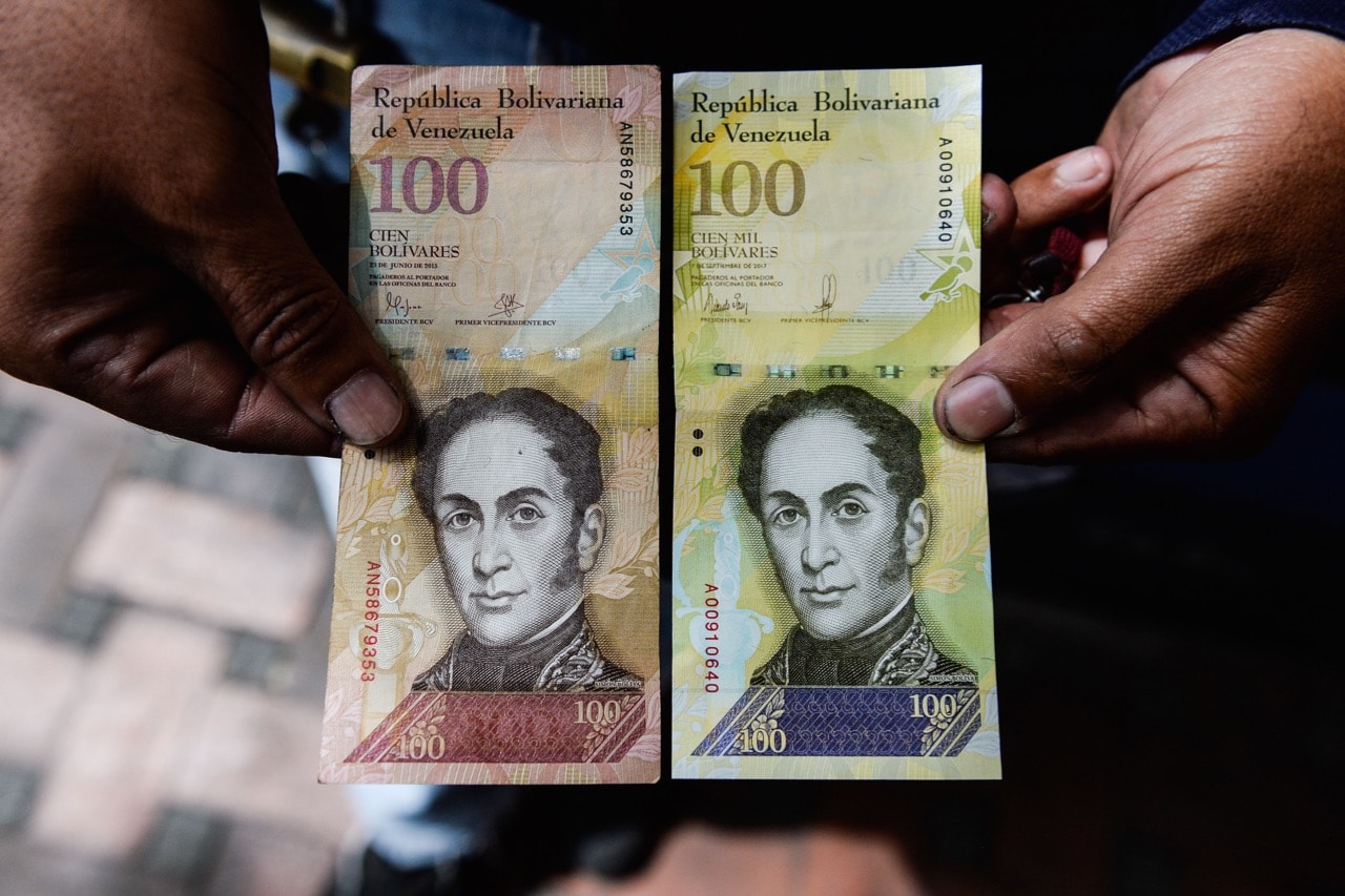 A man holds the new one hundred thousand-Bolivar-note (R) comparing it to the one hundred note, to show the resemblance between both bills in Caracas, 9 November 2017. At the time, the new bill was worth 29,89 US dollars in the official market and 2 dollars in the black market at November 9, 2017 exchange rate, FEDERICO PARRA/AFP/Getty Images