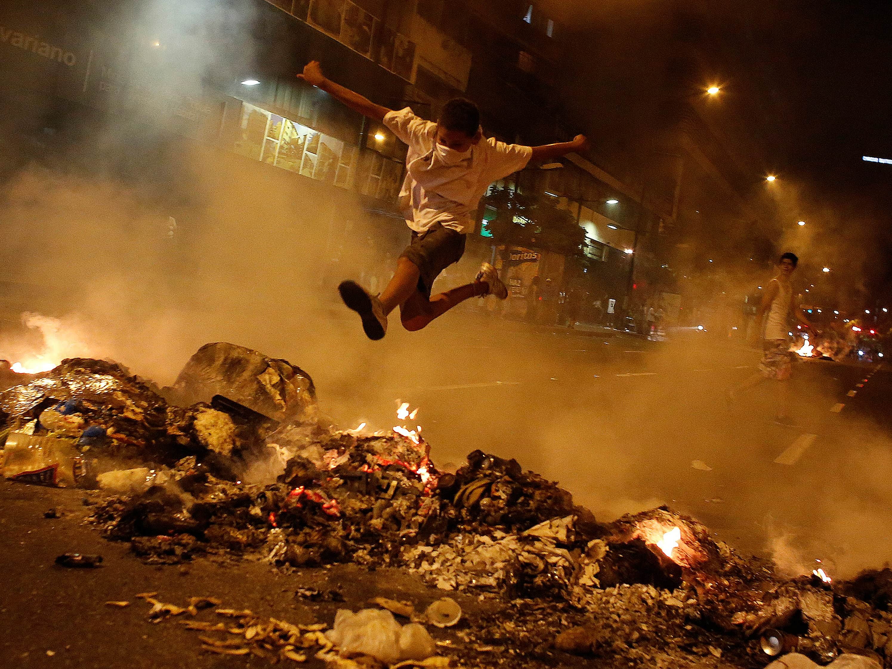 A boy jumps over a barricade of burning garbage that supporters of opposition leader Henrique Capriles used to block a street in Caracas, as they demonstrated for a recount of the votes in the presidential election, REUTERS/Tomas Bravo
