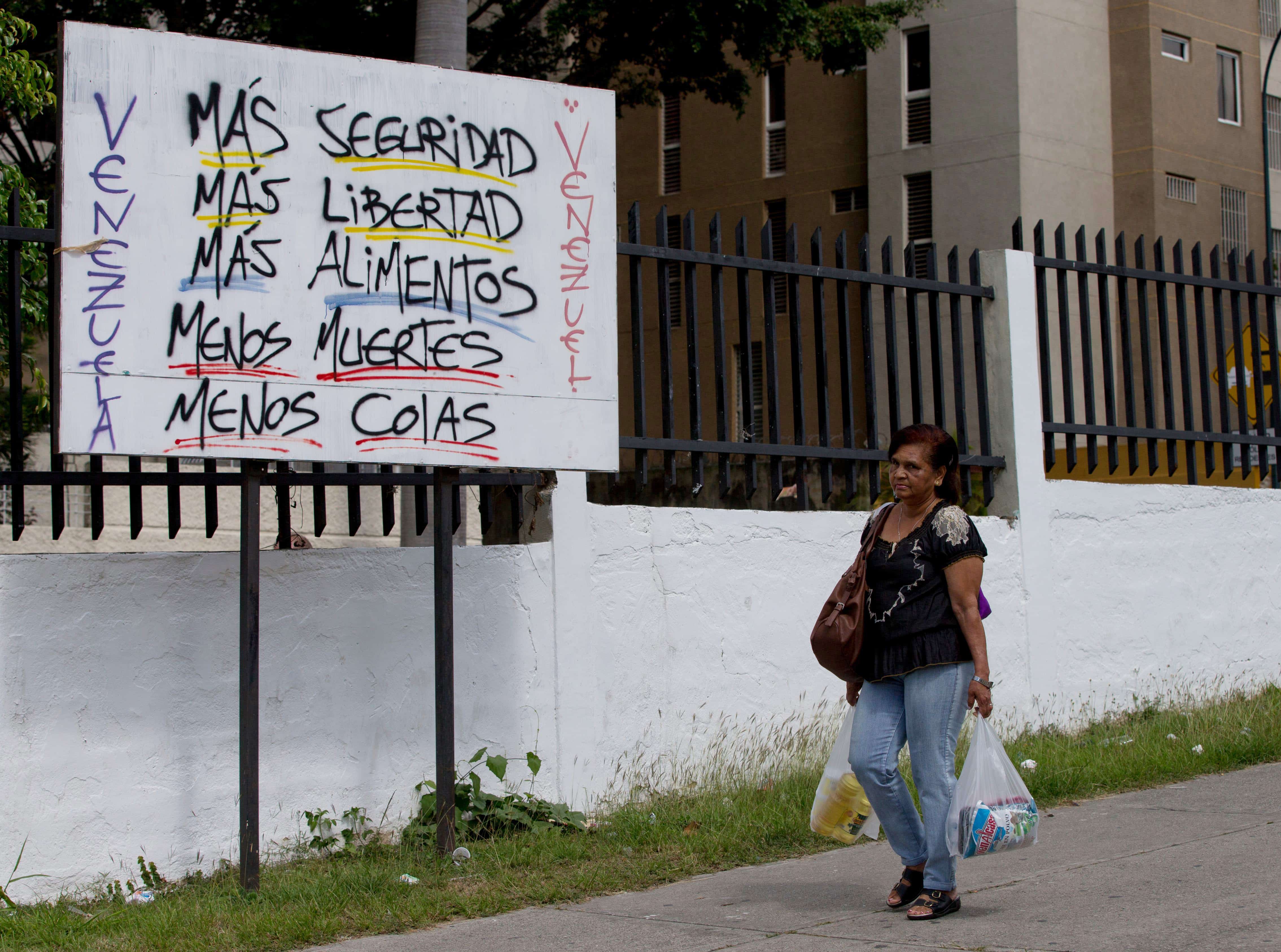 A woman walks by a poster that says "Venezuela, more security, more freedom, more food, fewer deaths, fewer lines" in Caracas, AP Photo/Fernando Llano