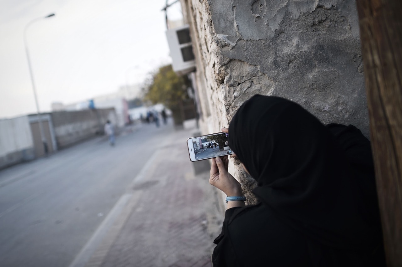 A Bahraini woman uses a mobile phone to take photos during clashes with riot police in the village of Sitra, south of the capital Manama, 8 January 2016, MOHAMMED AL-SHAIKH/AFP/Getty Images