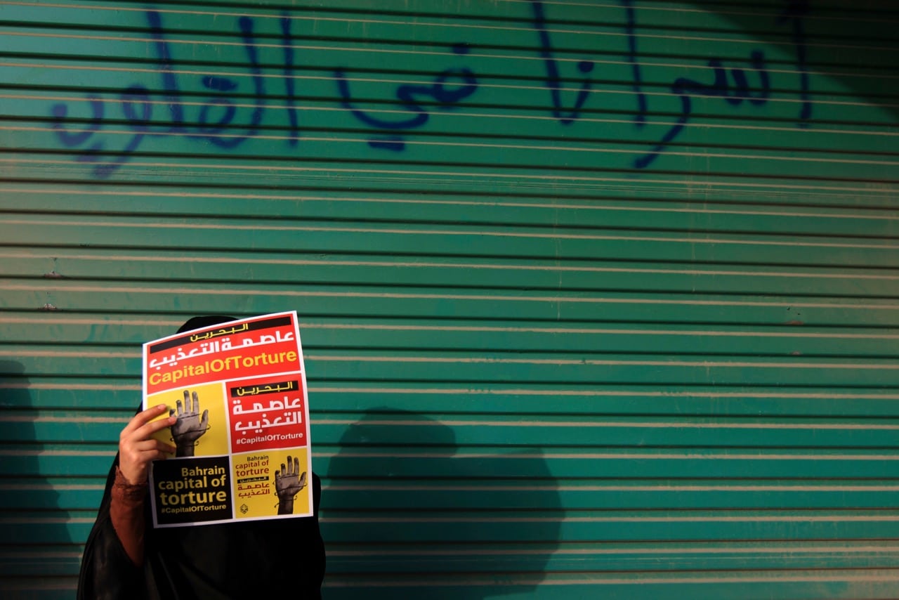 An anti-government protester carries a sign against torture during a march in Daih, Bahrain, 10 May 2013; the graffiti on the wall reads:" Our prisoners are in our hearts", AP Photo/Hasan Jamali
