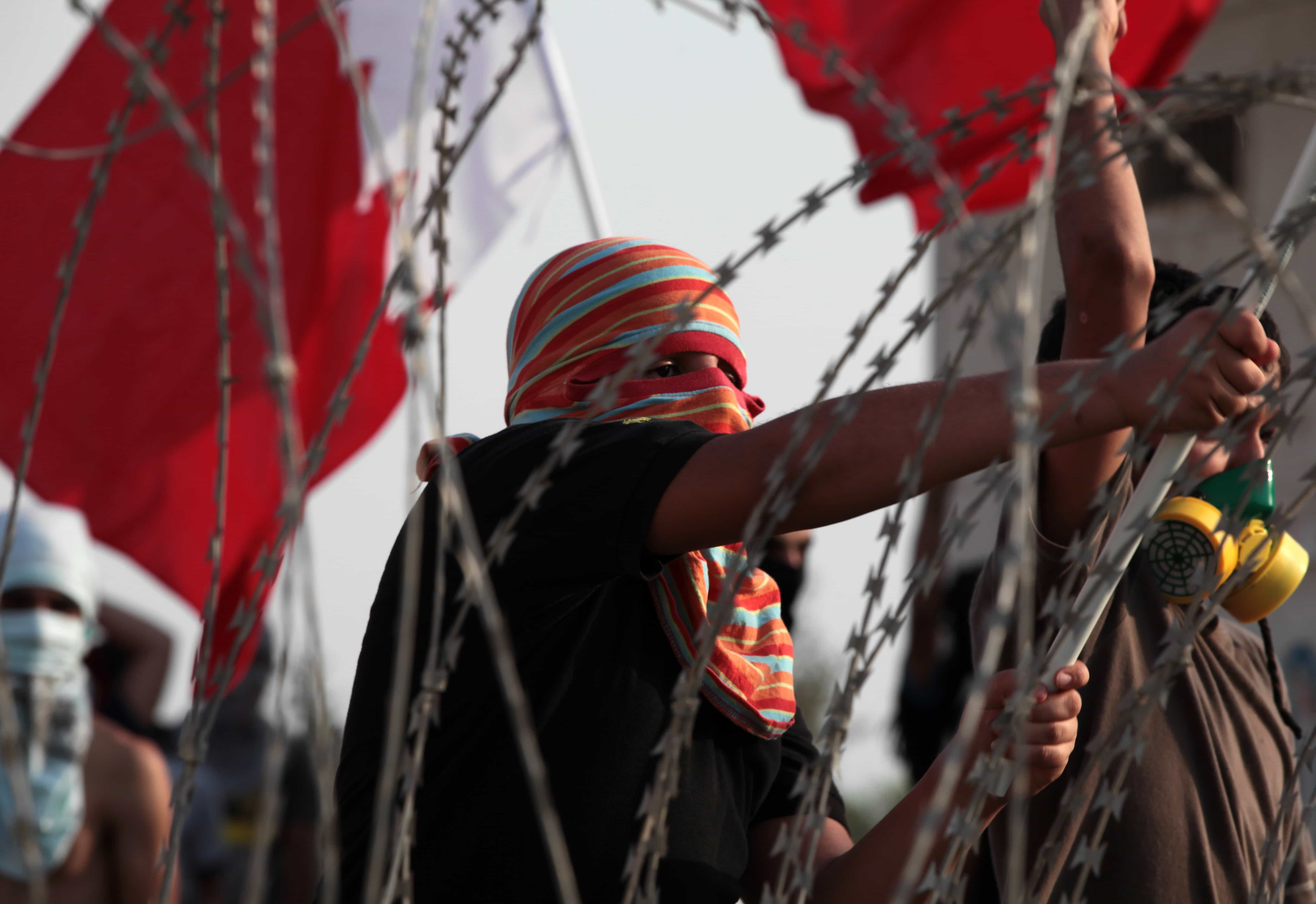 Protesters wave national flags toward riot police, unseen; razor wire was erected to prevent them from leaving their village to join other protests nationwide, AP Photo/Hasan Jamali