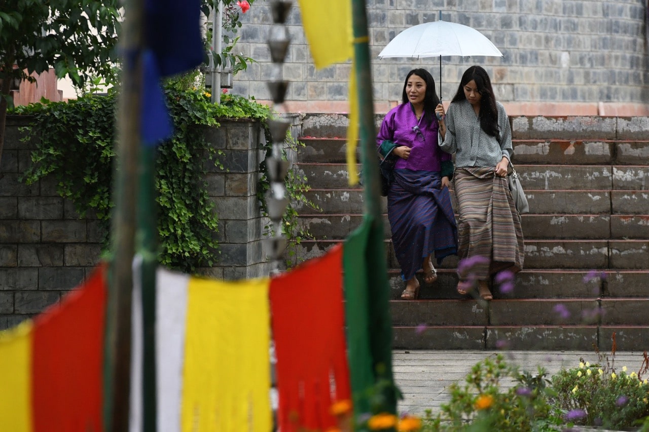 Two women shelter from the rain under an umbrella at the Royal University of Bhutan in Thimphu, 23 August 2018, ARUN SANKAR/AFP/Getty Images