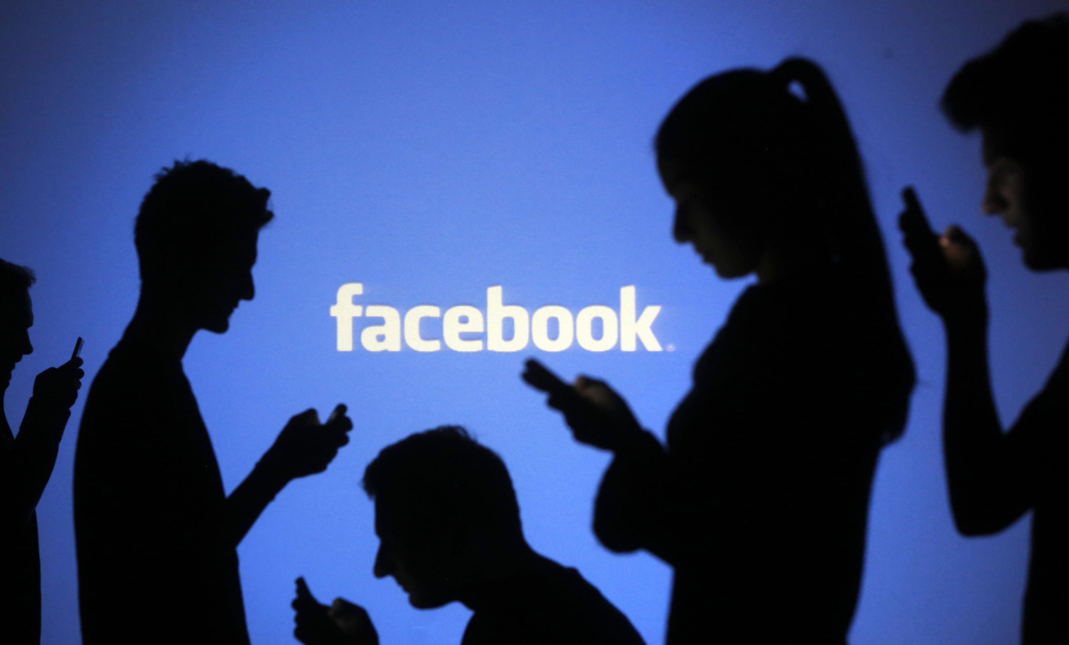 People are silhouetted as they pose with mobile devices in front of a screen projected with a Facebook logo, in Zenica, 29 October 2014, REUTERS/Dado Ruvic