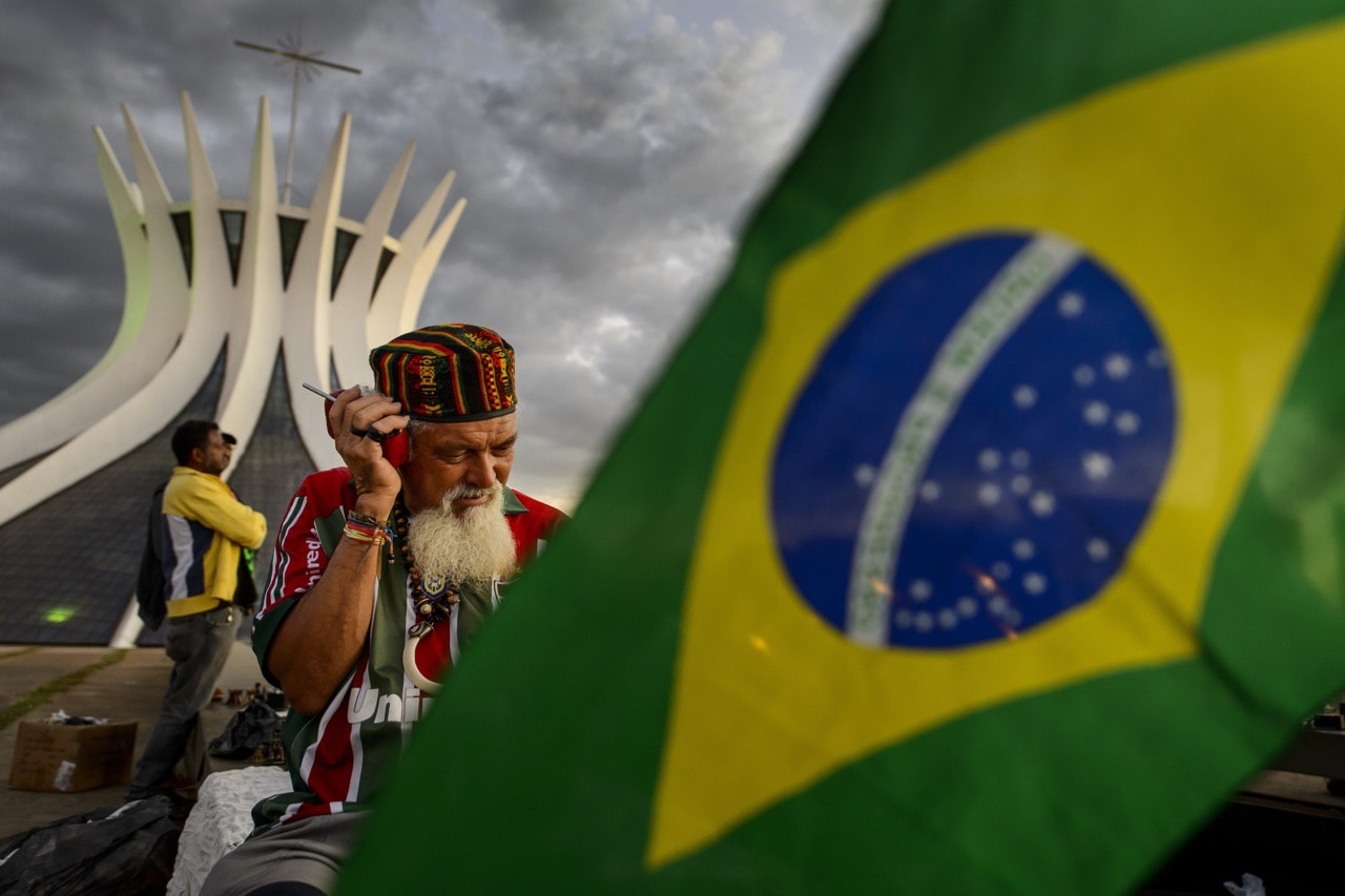 A vendor listens to the radio behind a Brazilian flag outside the Cathedral in Brasilia, 30 June 2014, FABRICE COFFRINI/AFP/Getty Images