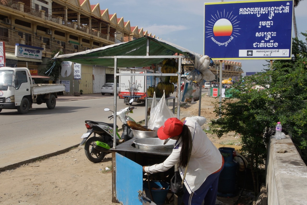 A vendor fries bananas at a sidewalk stall near a logo of the Cambodia National Rescue Party's (CNRP) outside Phnom Penh, 18 November 2017. Cambodia issued a public order to remove the CNRP logo, banners and slogans across the country, AP Photo/Heng Sinith