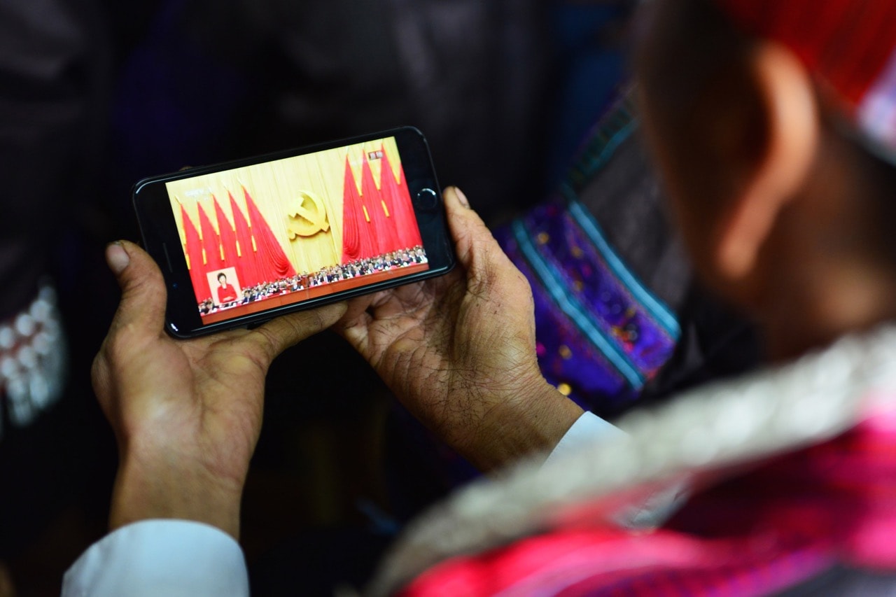 A woman of the Miao ethnic minority watches the opening session of the 19th Communist Party Congress on a smart phone in Jianhe, Guizhou province, China, 18 October 2017, STR/AFP/Getty Images