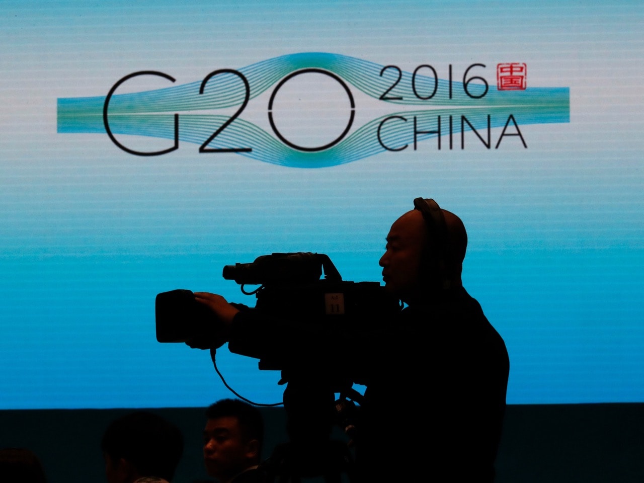 A cameraman is silhouetted near the G20 China summit logo in Hangzhou in eastern China's Zhejiang province, 5 September 2016, AP Photo/Ng Han Guan