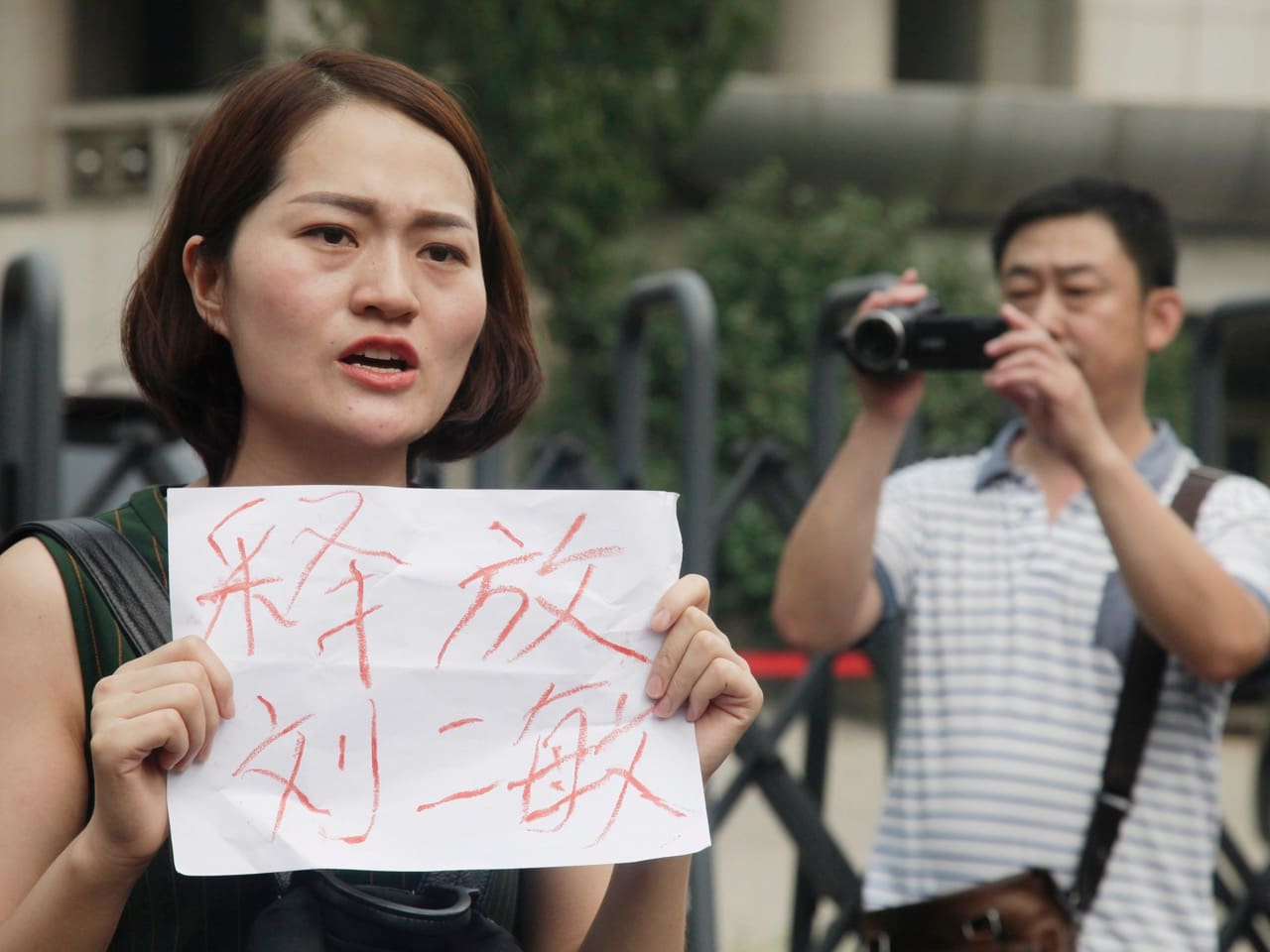 In this 1 August 2016 file photo, a man films Li Wenzu, wife of imprisoned lawyer Wang Quanzhang, during a protest outside a court in Tianjin, China, AP Photo/Gerry Shih, File