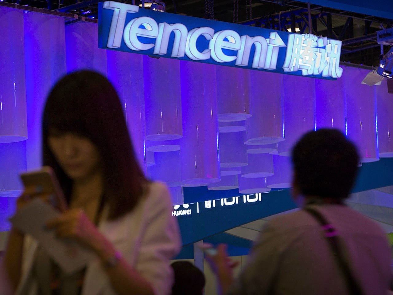 In this 29 April 2015 photo, a woman uses her smartphone near a booth for the Tencent company at the Global Mobile Internet Conference in Beijing, AP Photo/Mark Schiefelbein