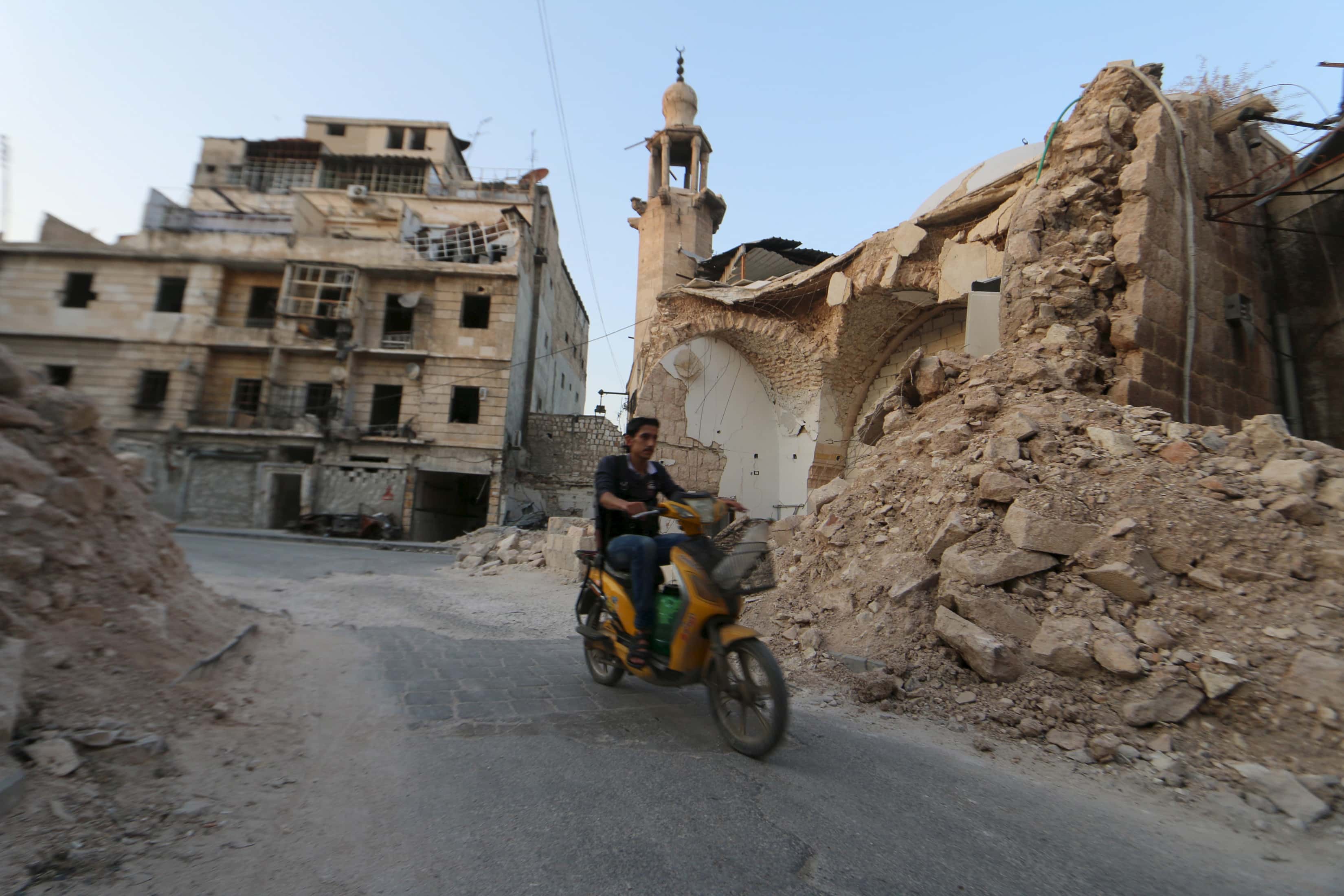 A man drives a motorcycle near damaged buildings in Aleppo, a city controlled partly by Islamic State and partly by Al-Nusra Front, on 15 July 2015, REUTERS/Abdalrhman Ismail