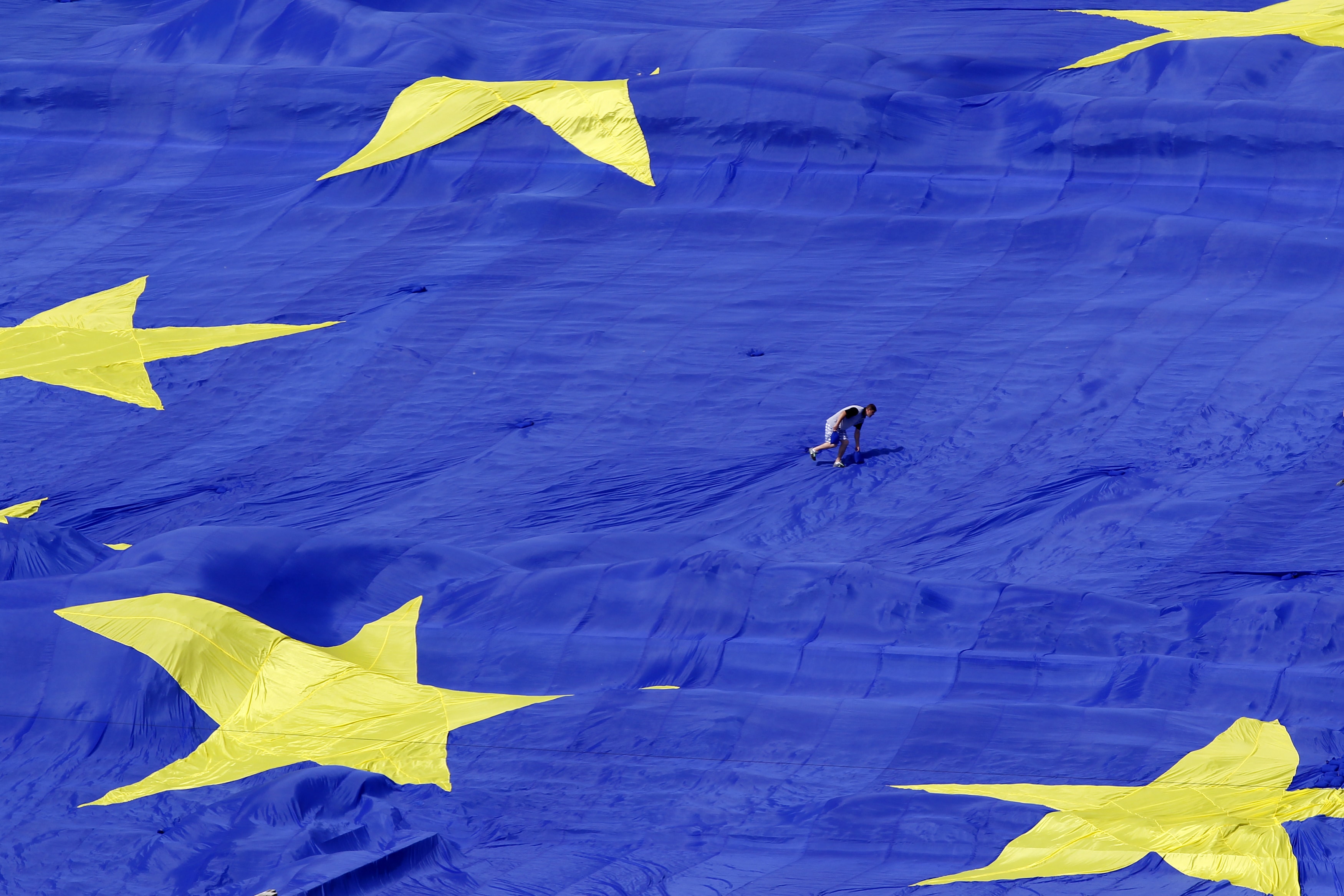 An organiser walks on a large European Union flag displayed in front of Romania's Parliament Building to mark EU Day in Bucharest, 9 May 2013., REUTERS/Bogdan Cristel