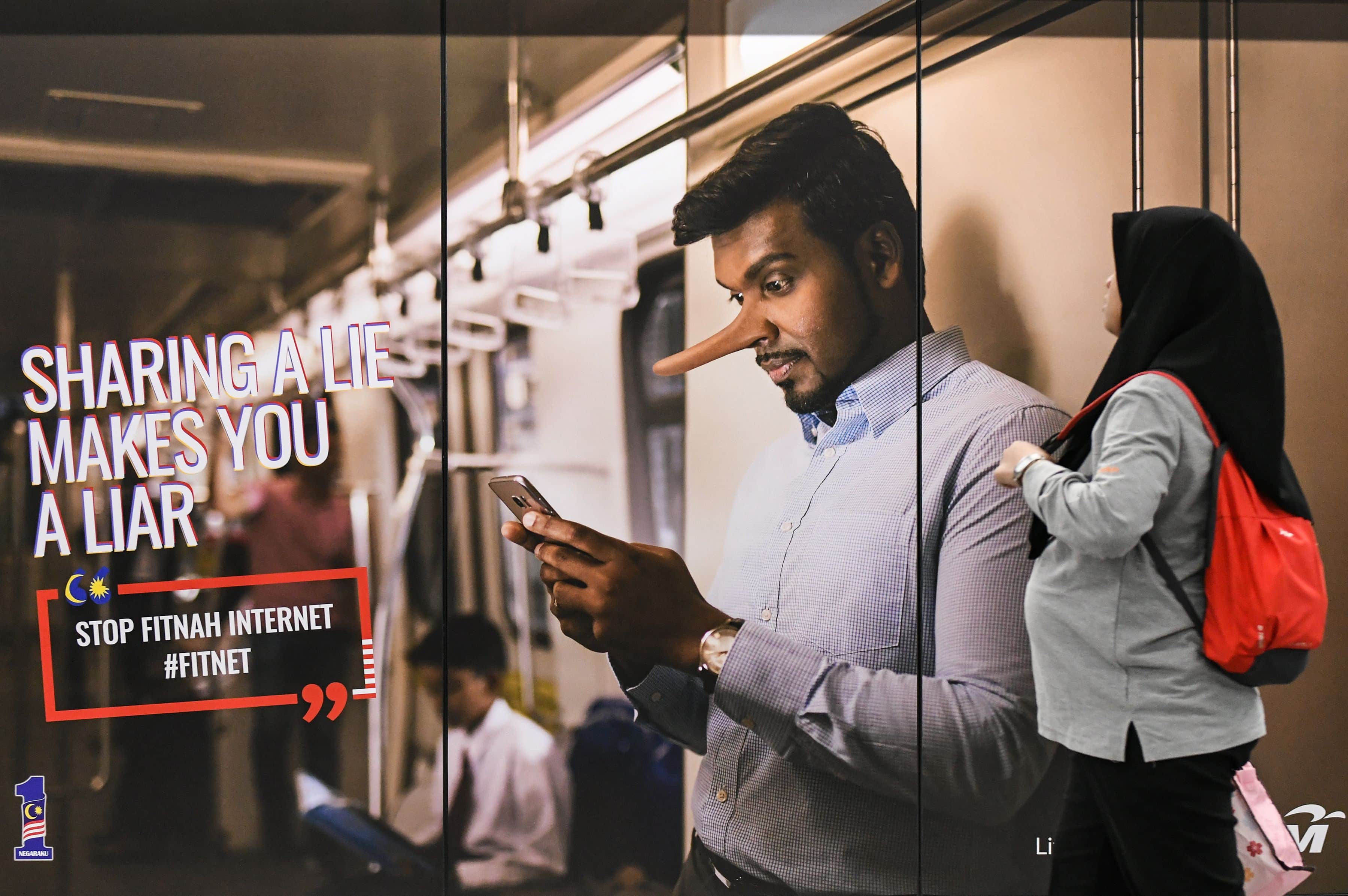 A commuter looks at an "Anti-Fake News" campaign poster in a downtown train station, Kuala Lampur, Malaysia, 26 March 2018, MOHD RASFAN/AFP/Getty Images