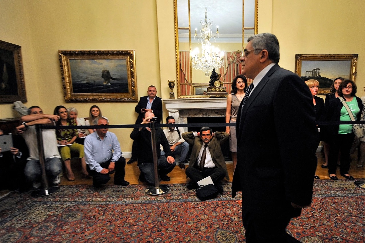 Journalists sit down in protest as the leader of the Golden Dawn party, Nikos Michaloliakos, arrives for a meeting with Greek President Carolos Papoulias (unseen) at the Greek Parliament in Athens, 13 May 2012, LOUISA GOULIAMAKI/AFP/GettyImages