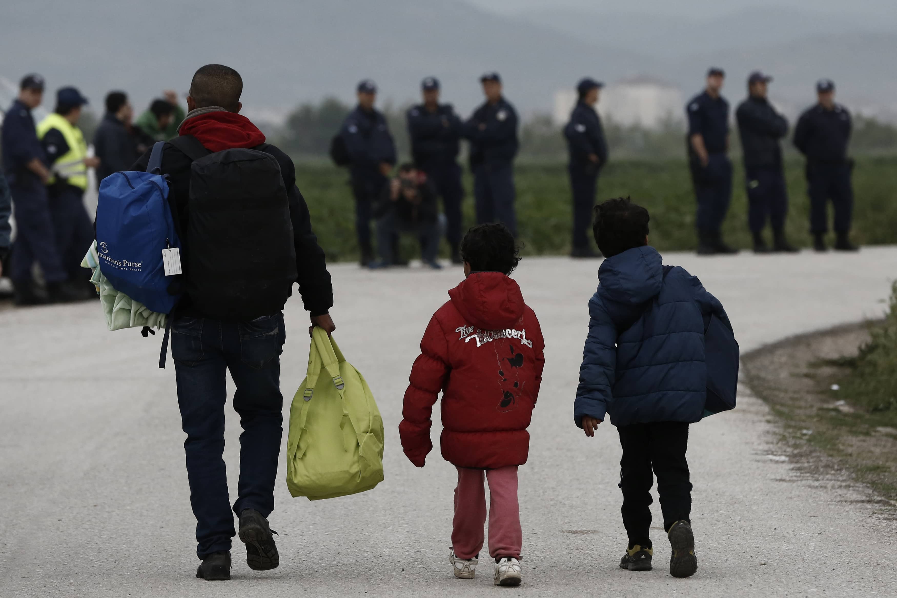 Refugees carry their belongings in front of riot policemen during a police operation at a refugee camp at the border between Greece and Macedonia, near the village of Idomeni, Greece, 24 May 2016. , REUTERS/Yannis Kolesidis/Pool