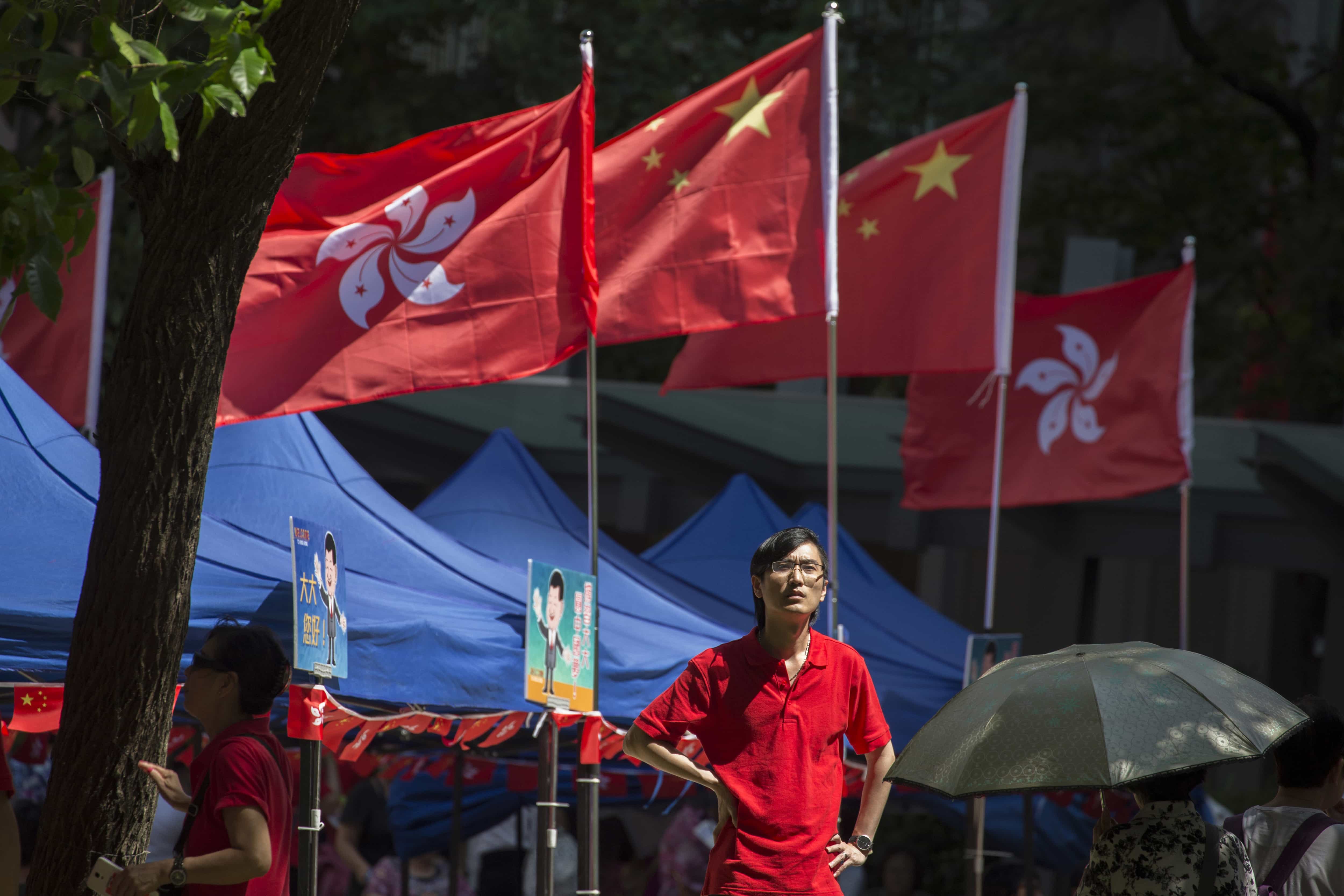 A man stands near Chinese and Hong Kong flags at an event to show support for the Chinese president's visit at a gathering in Hong Kong, 29 June 2017, AP Photo/Ng Han Guan