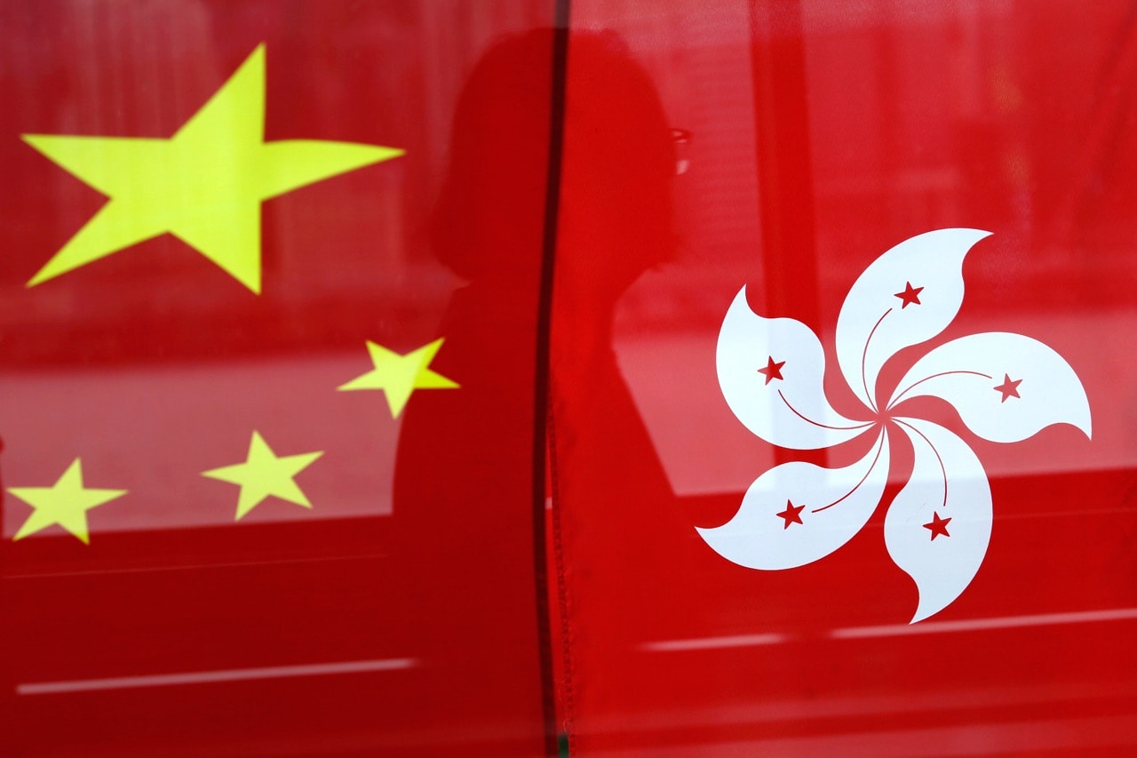 A woman is reflected in a window behind Chinese and Hong Kong flags, in Hong Kong, 2 July 2017, REUTERS/Tyrone Siu