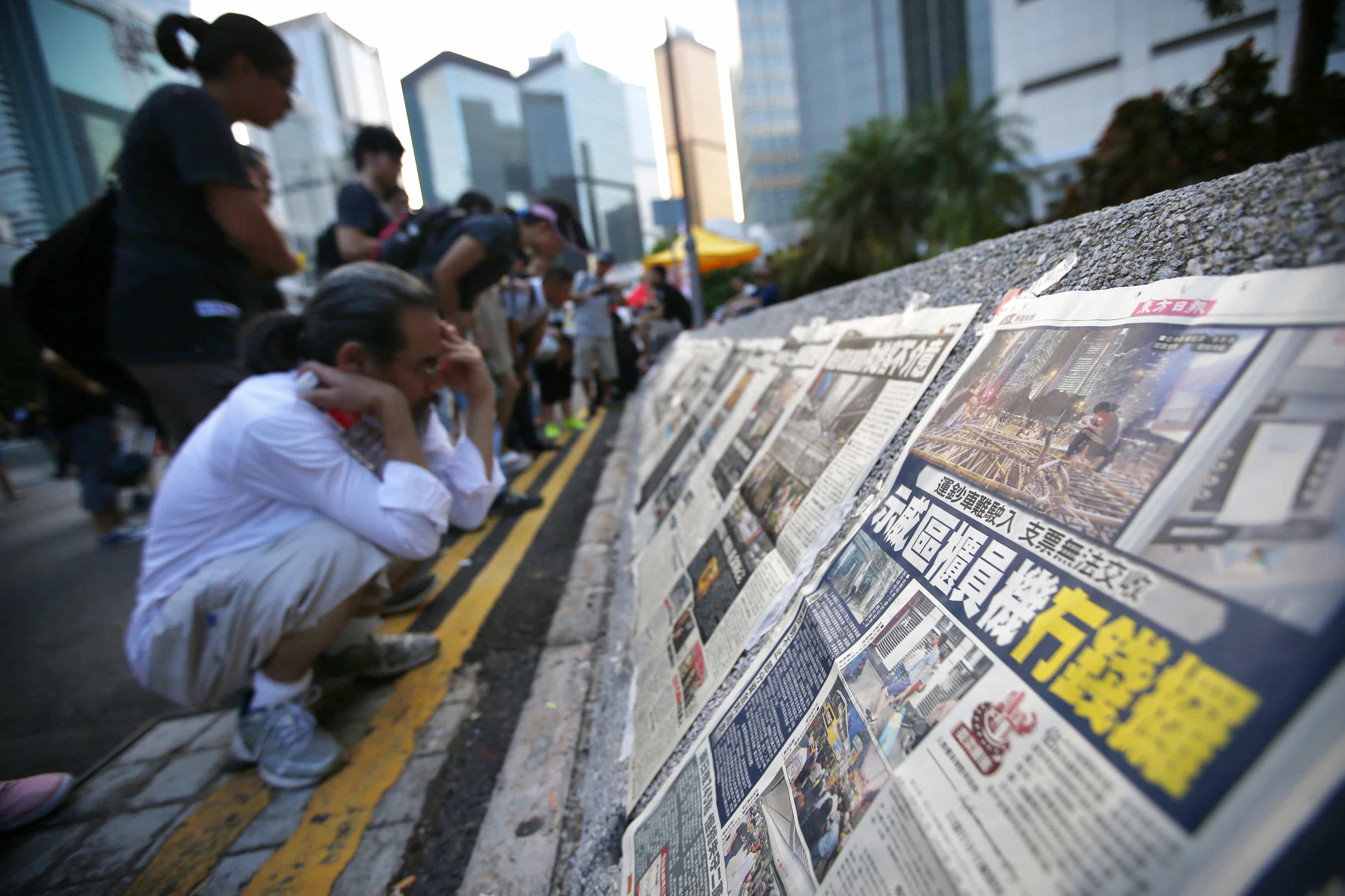 People read newspapers on a street blocked by protesters outside of the government headquarters building in Hong Kong, 1 October 2014, REUTERS/Carlos Barria