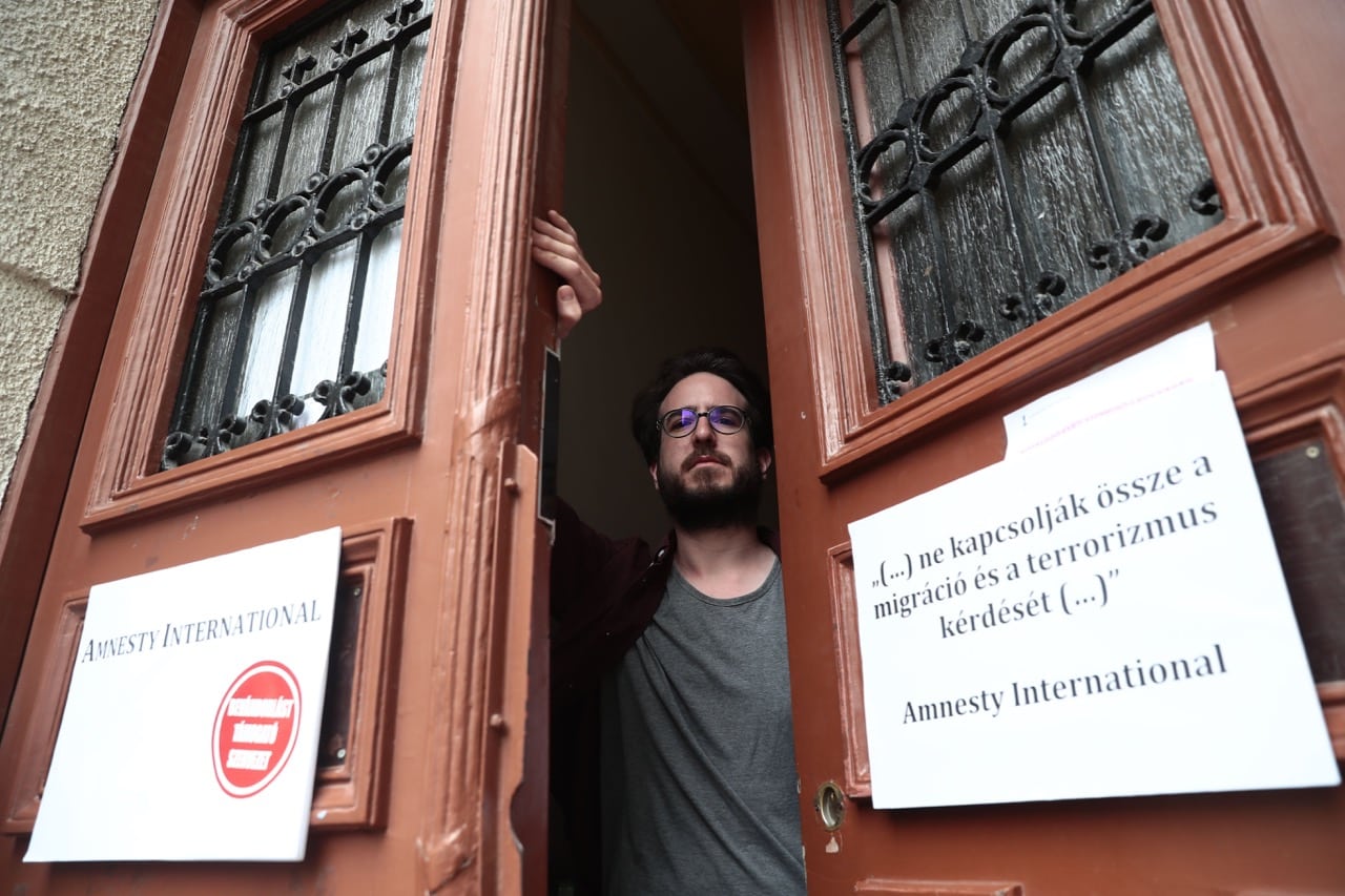 Aron Demeter, Amnesty International press officer, poses next to posters that were placed on the office's door by members of the youth wing of the Fidesz party in Budapest, Hungary, 27 June 2018; the posters read (in the red dot) 'organisation supporting immigration' and (R) '(...) Do not connect the question of Migration and Terrorism (...), FERENC ISZA/AFP/Getty Images